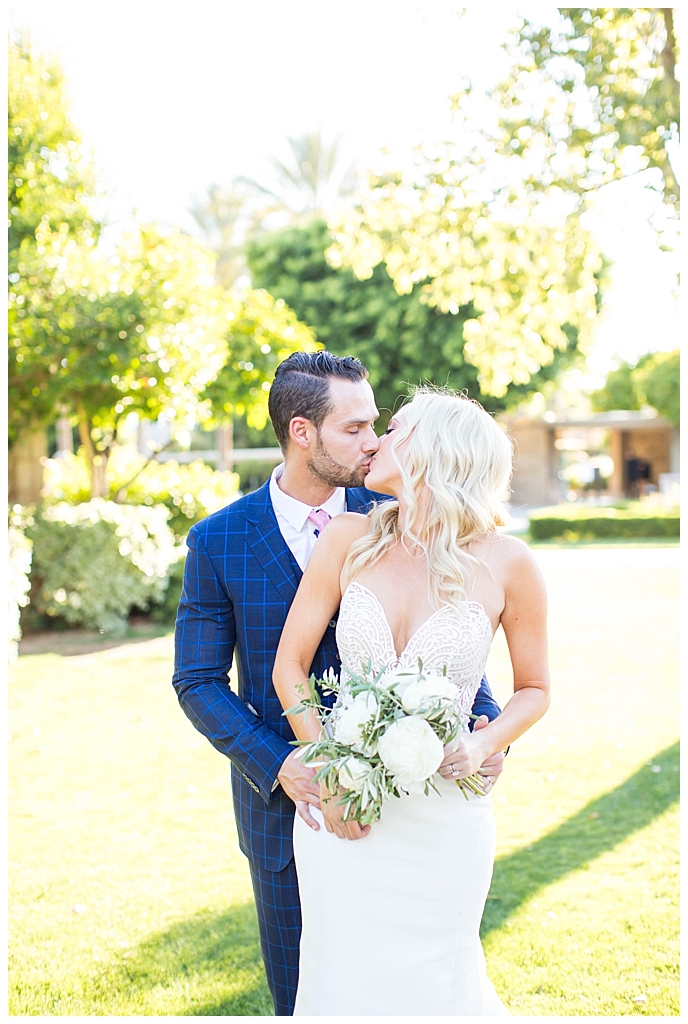 bride in two piece wedding dress and groom in custom blue suit kissing at Arizona Biltmore