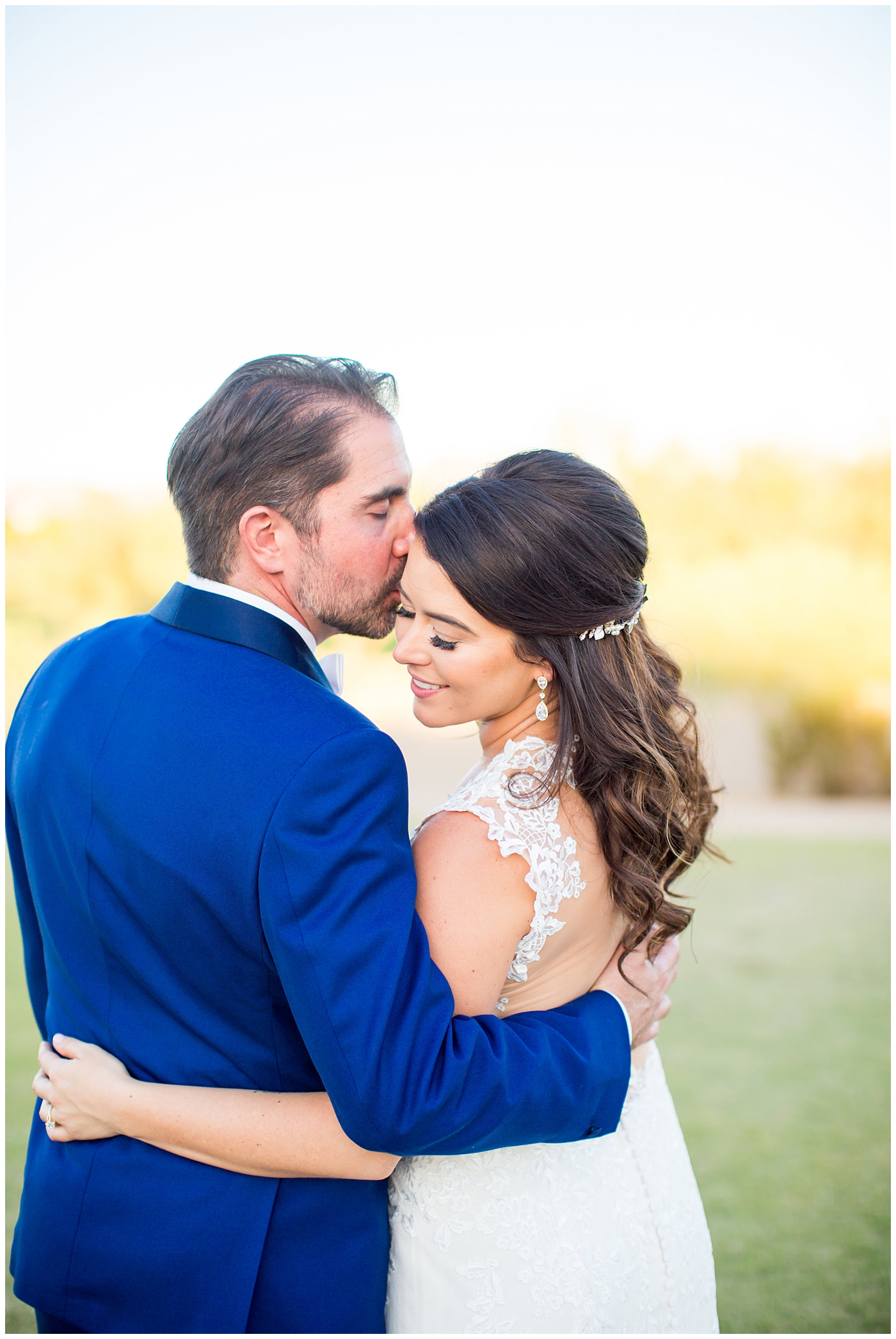 Bride in Justina Alexander dress with groom in custom blue suit kissing her cheek