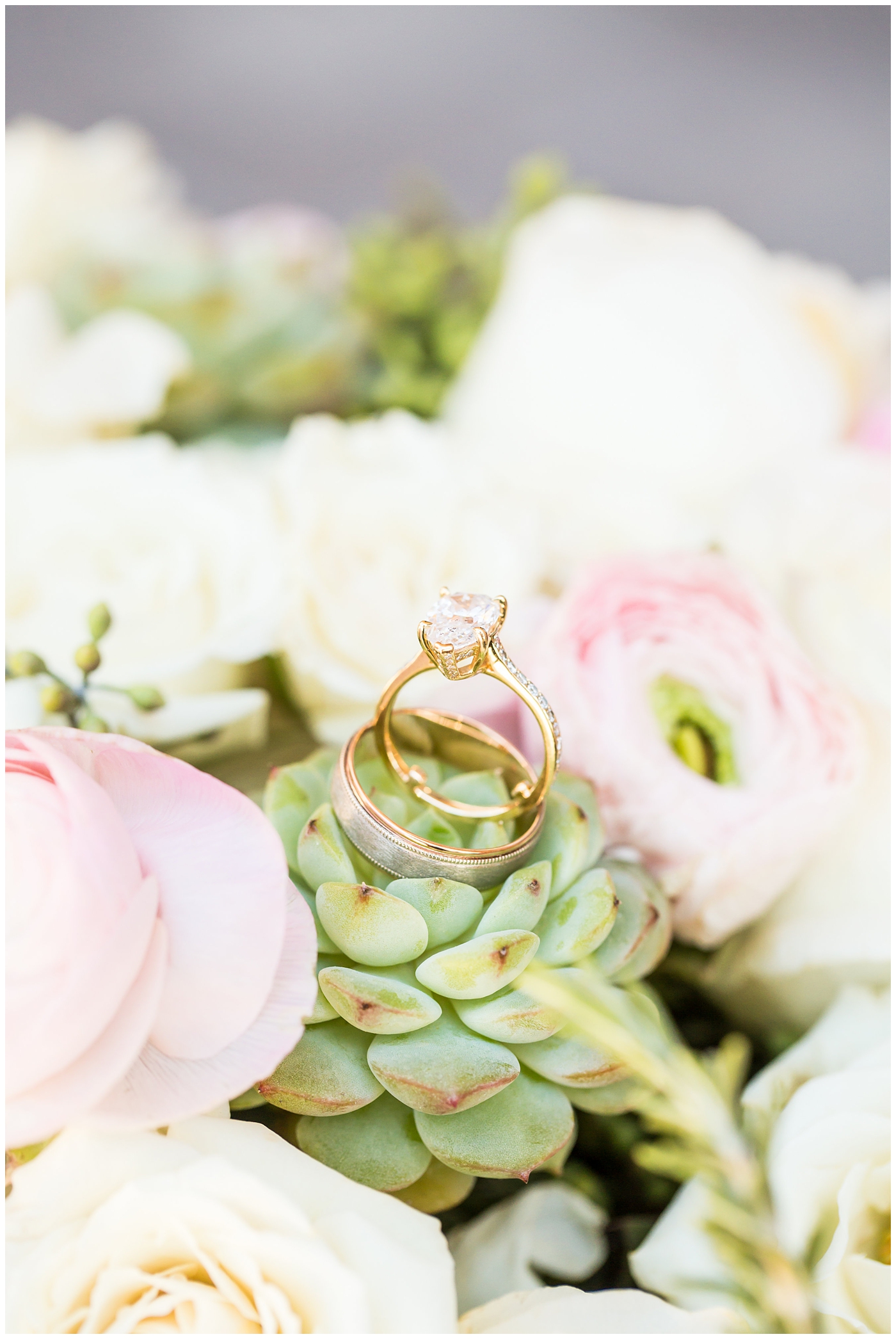 Wedding rings on bride's white rose, pink ranunculus, and green succulents