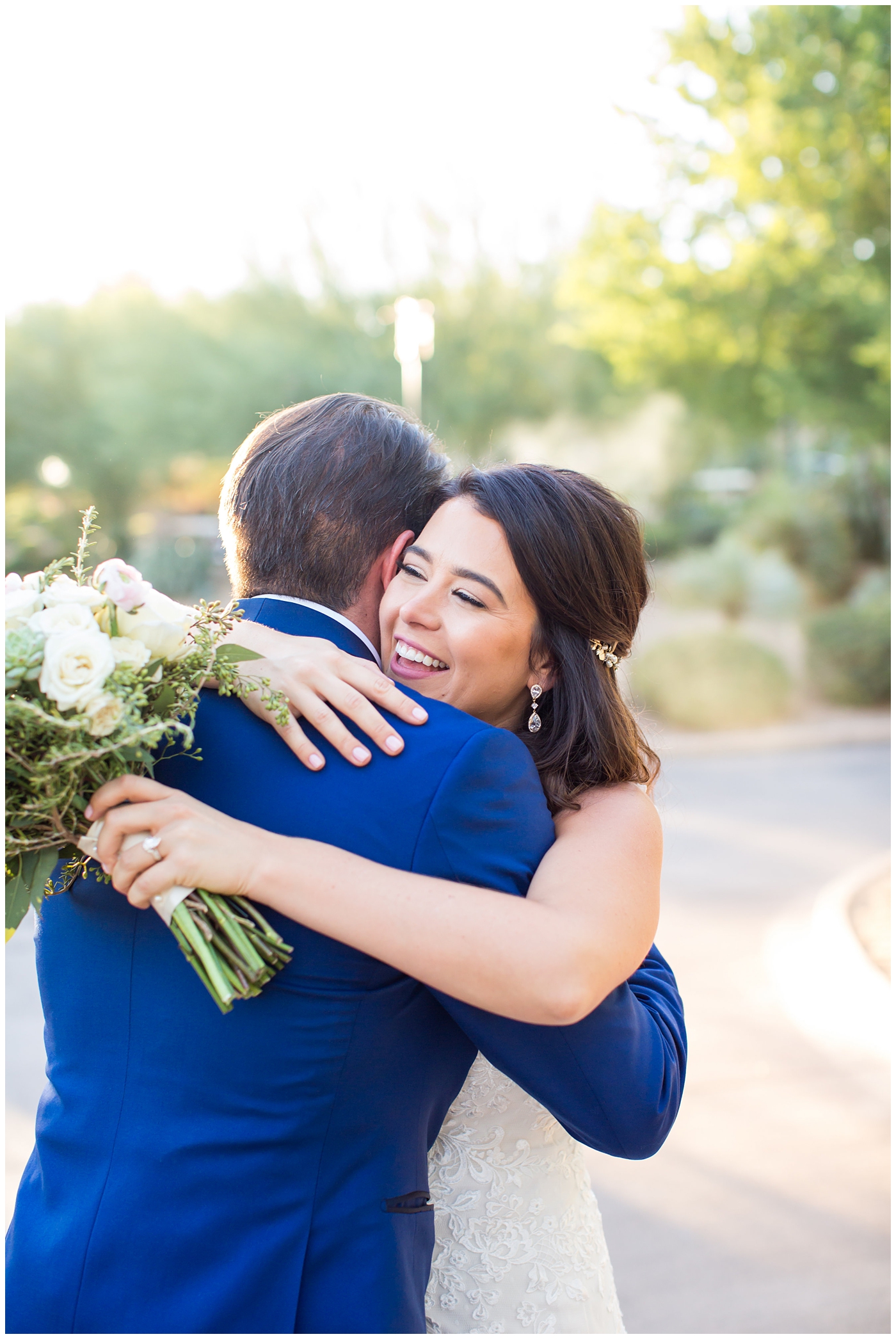 Bride in Justina Alexander dress with groom in custom Brother's Tailors blue suit hugging after first look