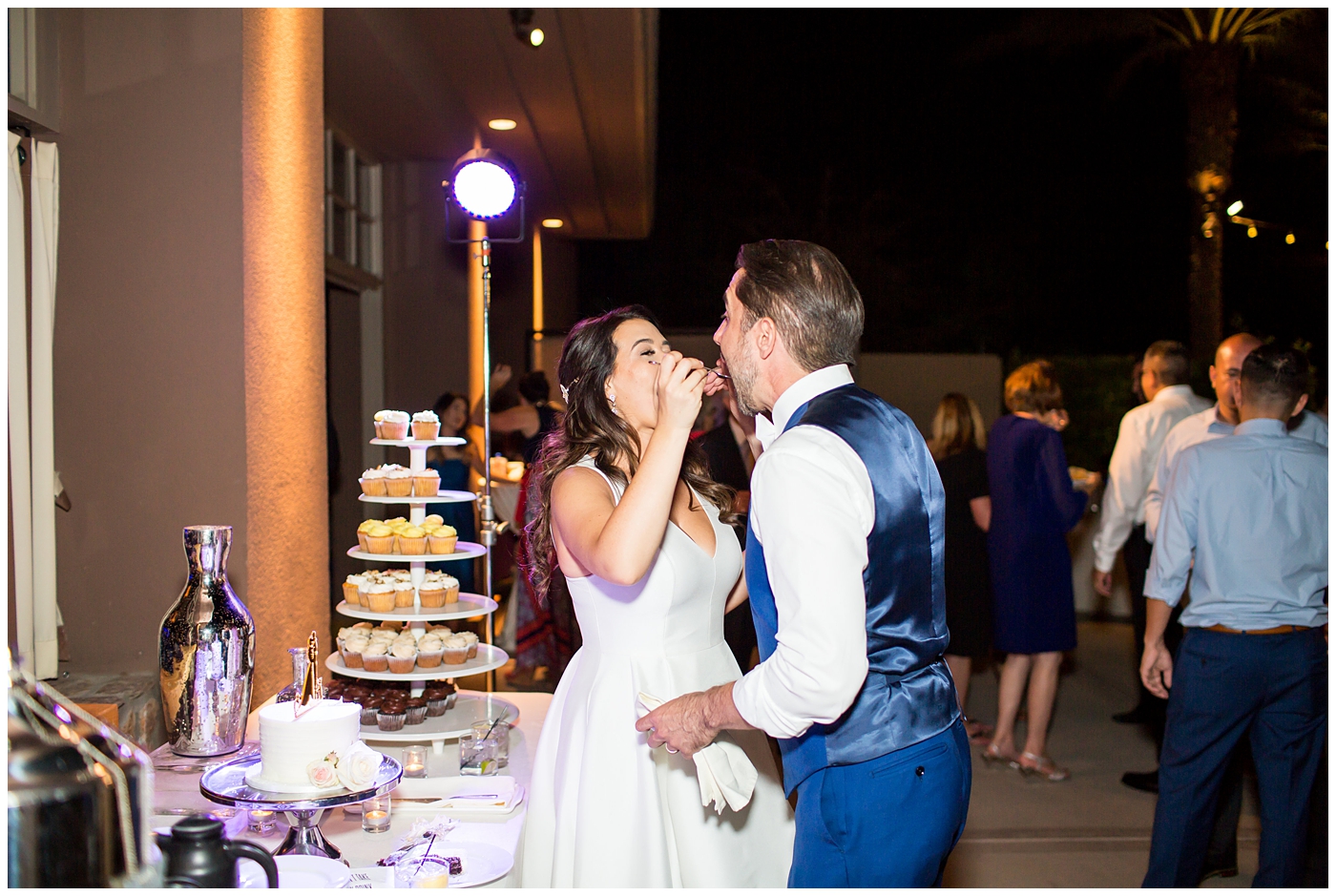 Bride in Justina Alexander dress with groom in custom Brother's Tailors blue suit cake cutting