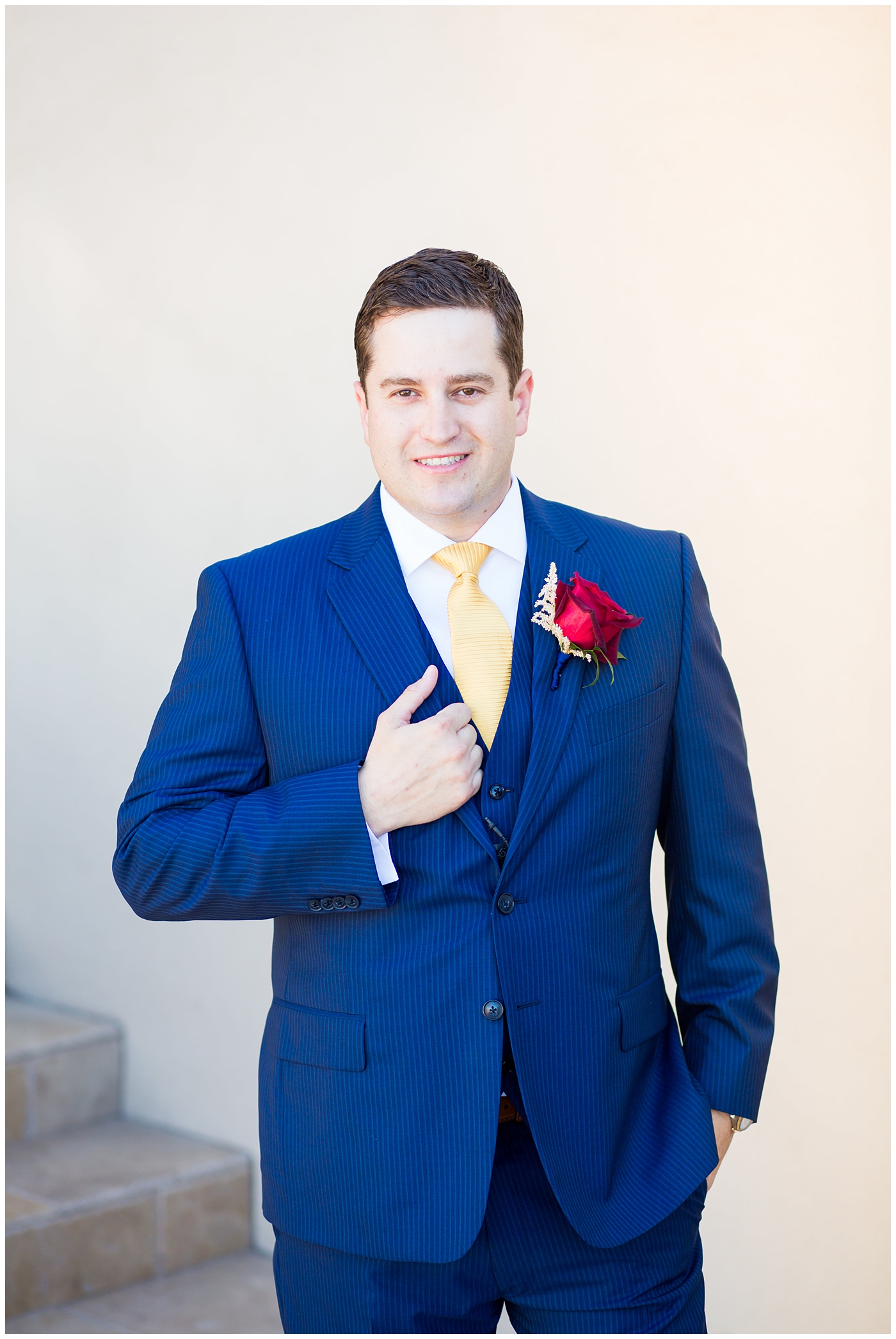 groom in blue suit with yellow tie and red rose boutonniere
