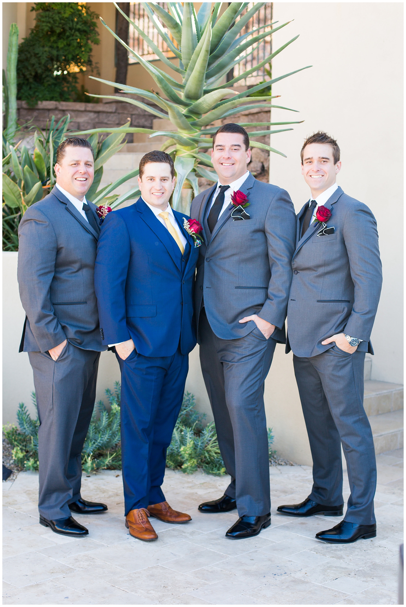 groom in blue suit with yellow tie and red rose boutonniere and groomsmen in gray suits
