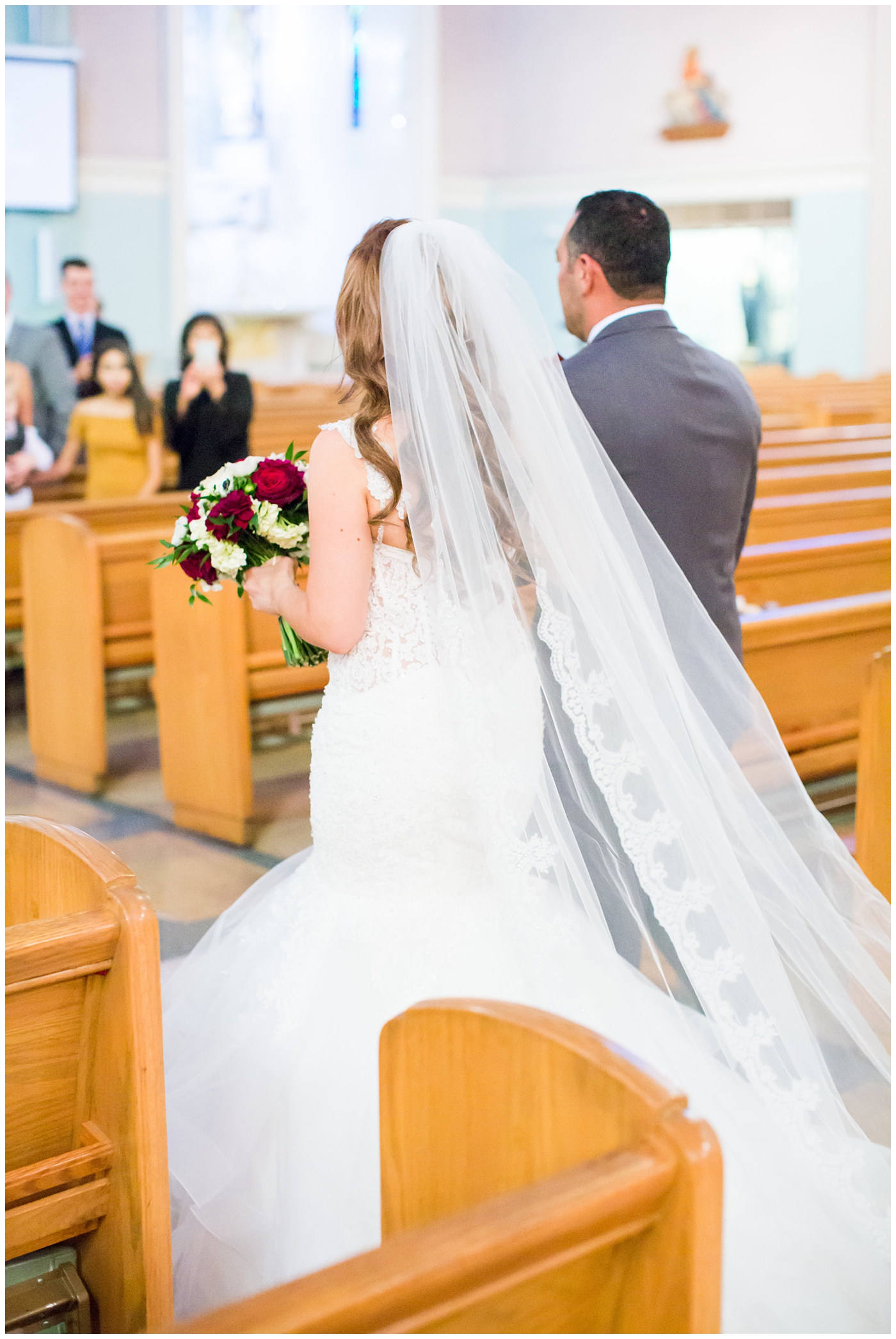 bride in morilee wedding dress with red and white rose bouquet walking down the aisle