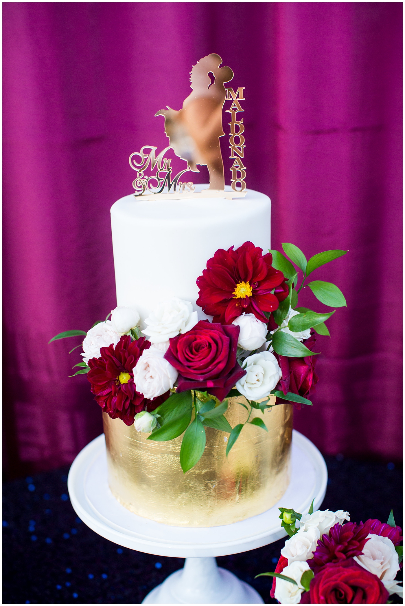wedding cake with gold cutout topper and red and white florals