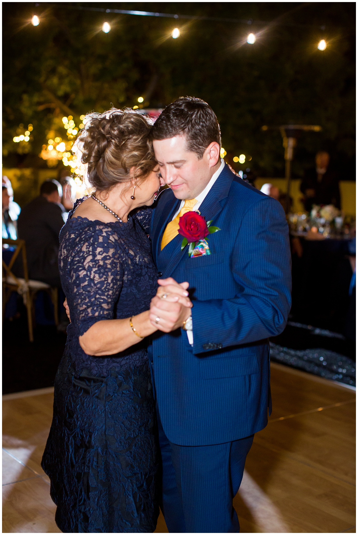 groom in blue suit with yellow tie and red rose boutonniere dance with mother