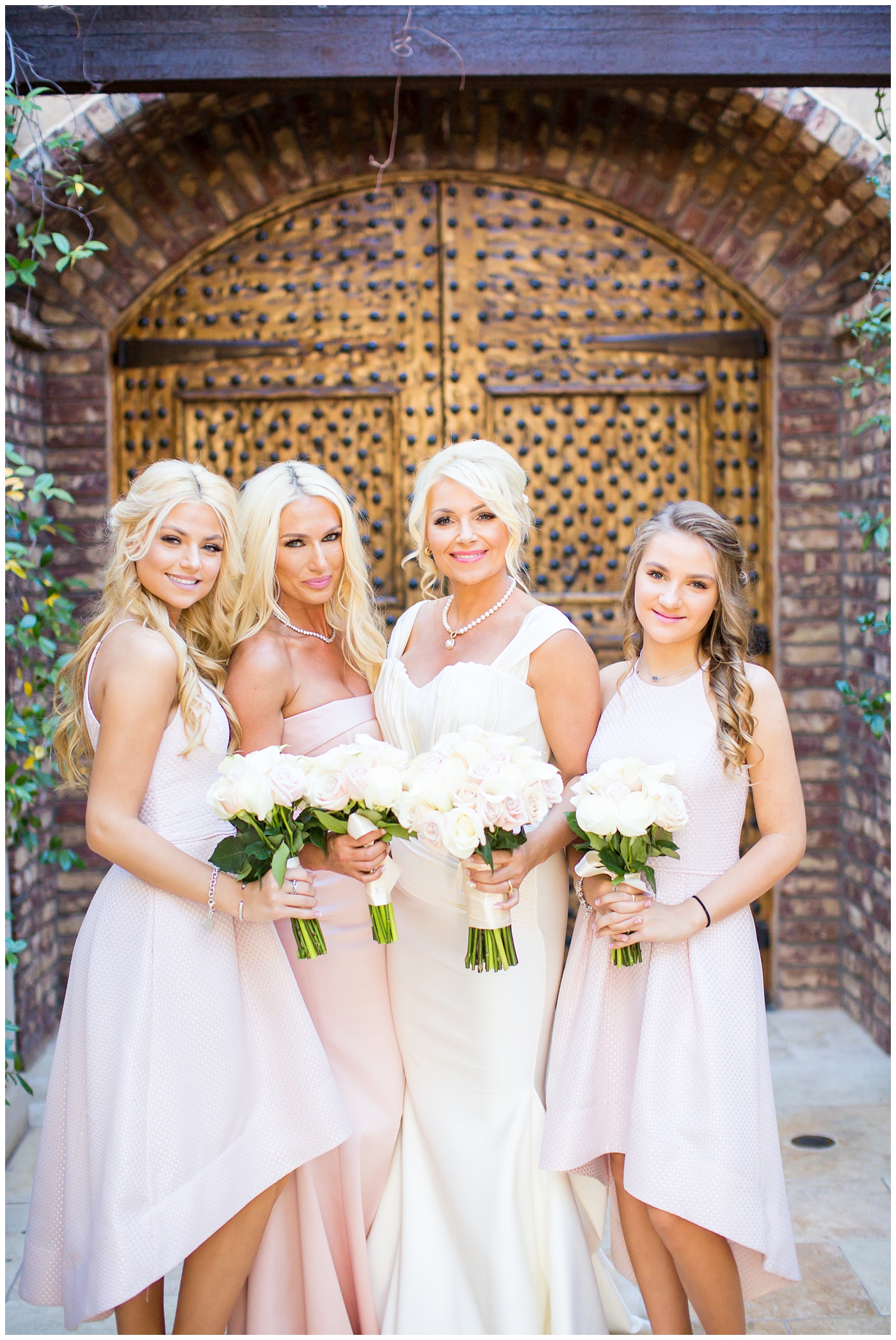 bride in cap sleeve wedding dress with bridesmaids holding rose bouquets