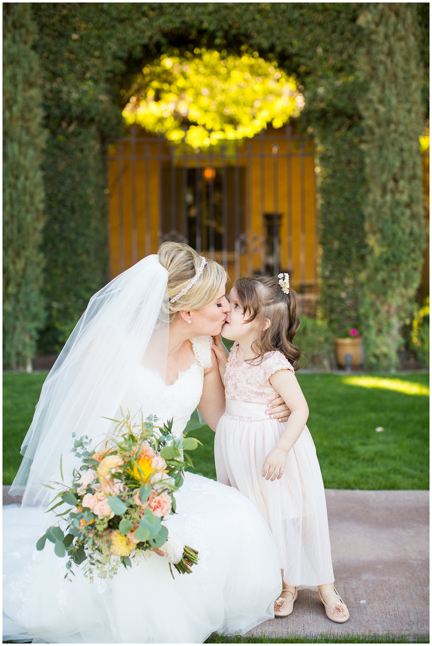 bride in essence designs wedding dress with cap sleeves with bridal bouquet with orange roses, greenery, yellow flowers bridal portrait with flower girl in pink dress