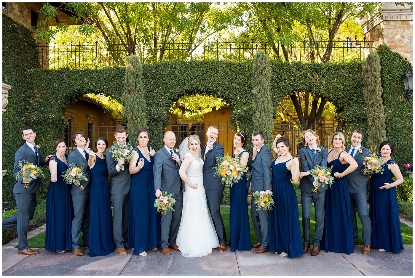 bride in essence designs wedding dress with cap sleeves portrait group shot with bridesmaids in navy blue long dresses with groom in gray suit with pink tie and groomsmen in gray suits with blue ties