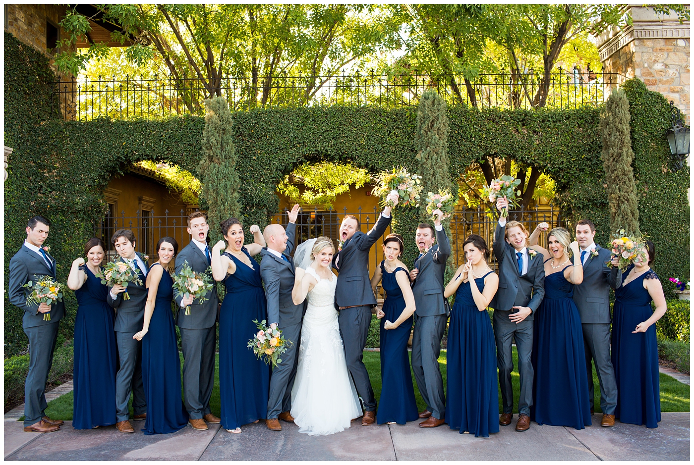bride in essence designs wedding dress with cap sleeves portrait group shot with bridesmaids in navy blue long dresses with groom in gray suit with pink tie and groomsmen in gray suits with blue ties