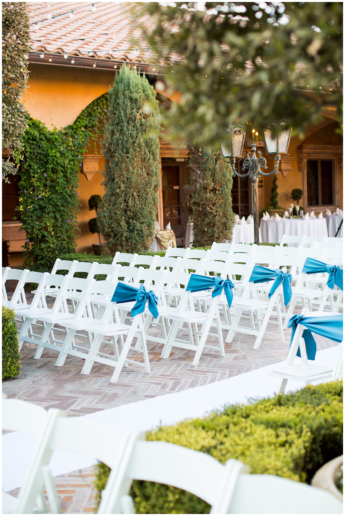 courtyard wedding ceremony with white folding chairs with blue ribbon