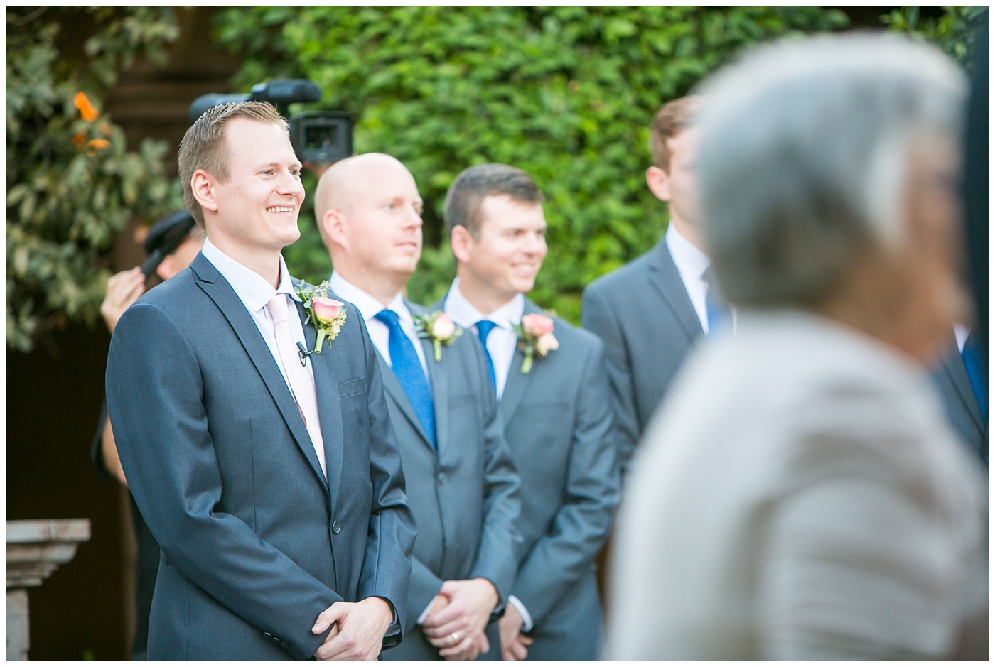 groom in gray suit with pink tie seeing bride walk down the aisle at wedding ceremony