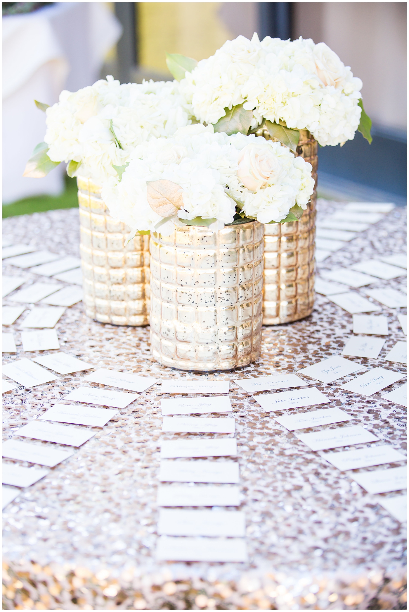 gold vase with white roses on rose gold sequin linen table escort card display