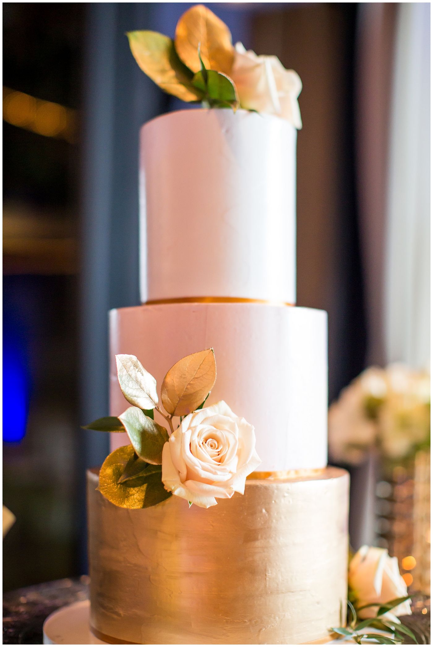 blush pink and gold three layer tier cake with white roses at wedding reception