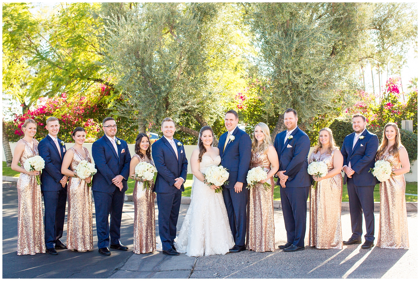 bride in lillian lottie couture wedding dress with white rose bouquet and groom in navy blue suit from men's warehouse with wedding party