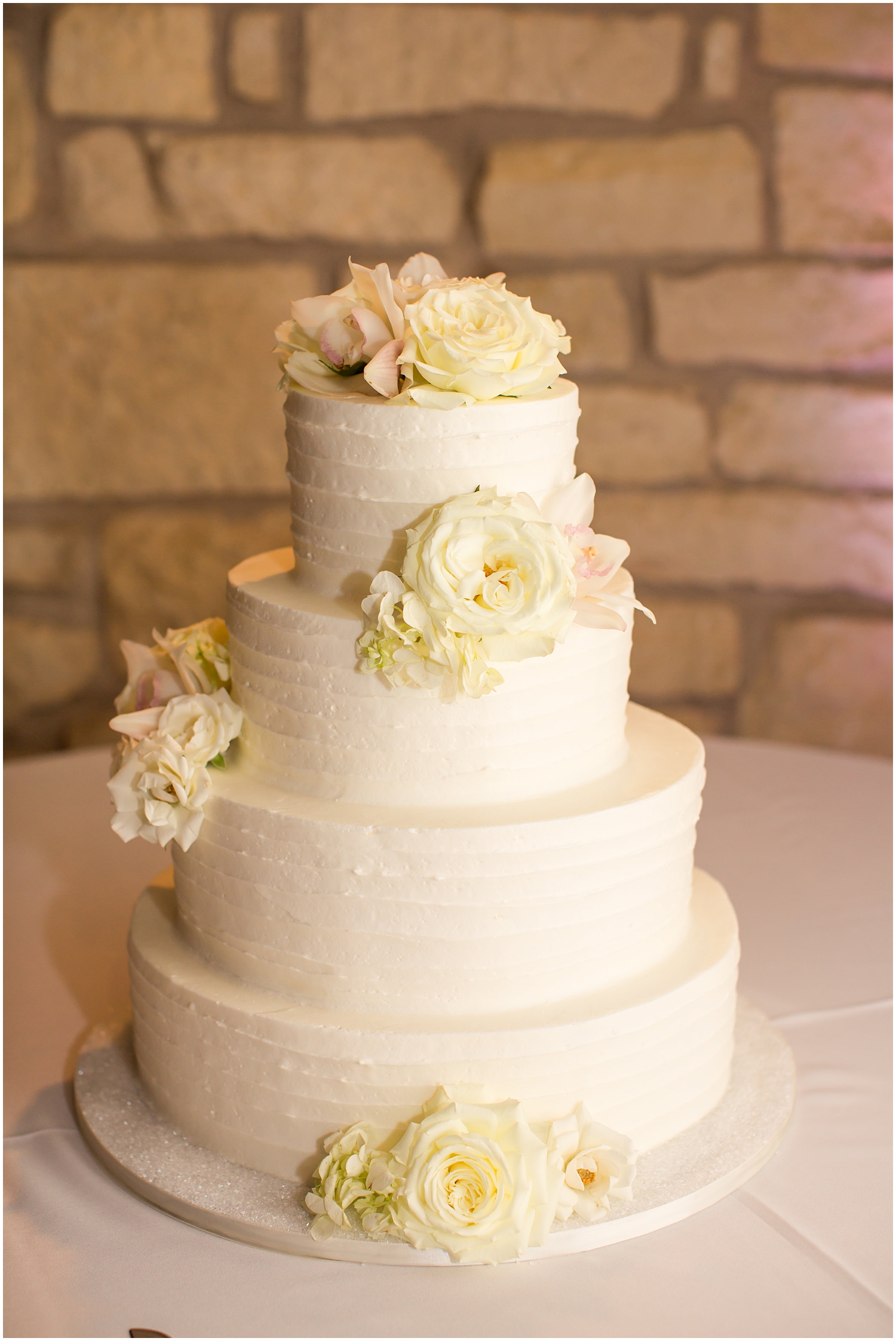 four tier white wedding cake with frosting texture and white roses and hydrangeas for wedding day reception