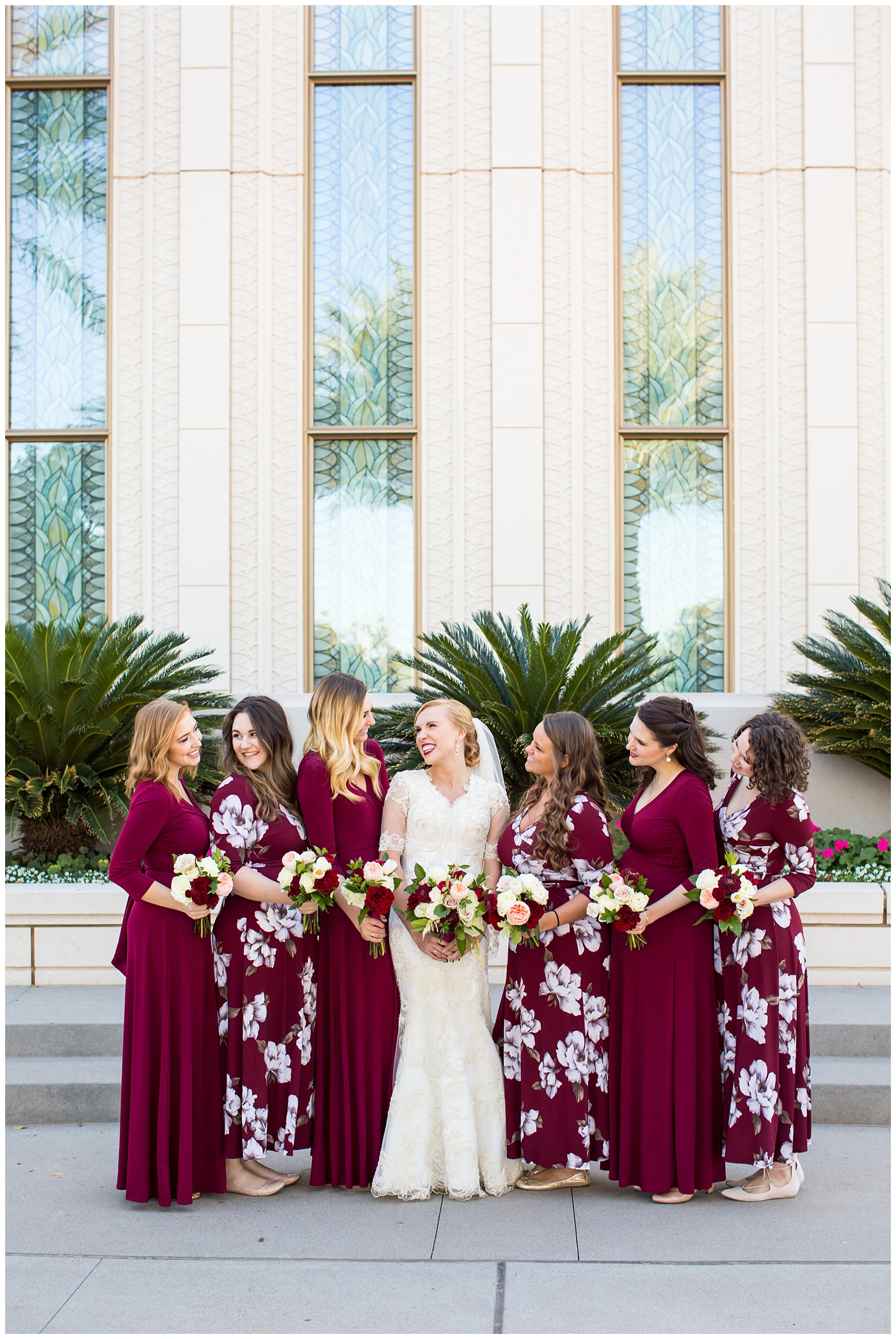 bride in sleeved lace dress with burgundy, white, and green wedding bouquet with bridesmaids in long sleeve burgundy and floral dresses wedding day portrait at Gilbert LDS temple