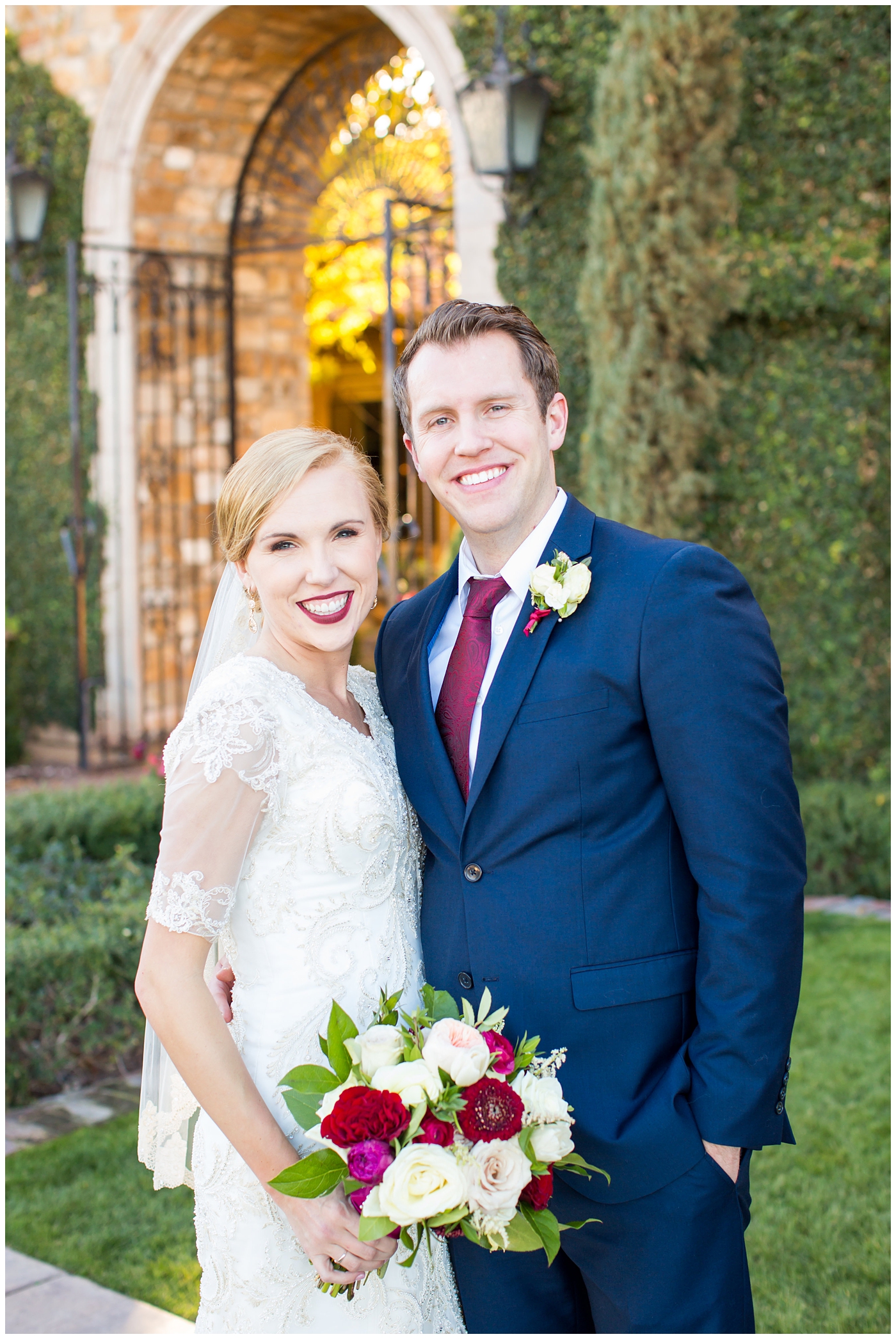 bride in sleeved lace dress with burgundy, white, and green wedding bouquet and groom in navy suit with burgundy tie wedding day portrait at Villa Siena