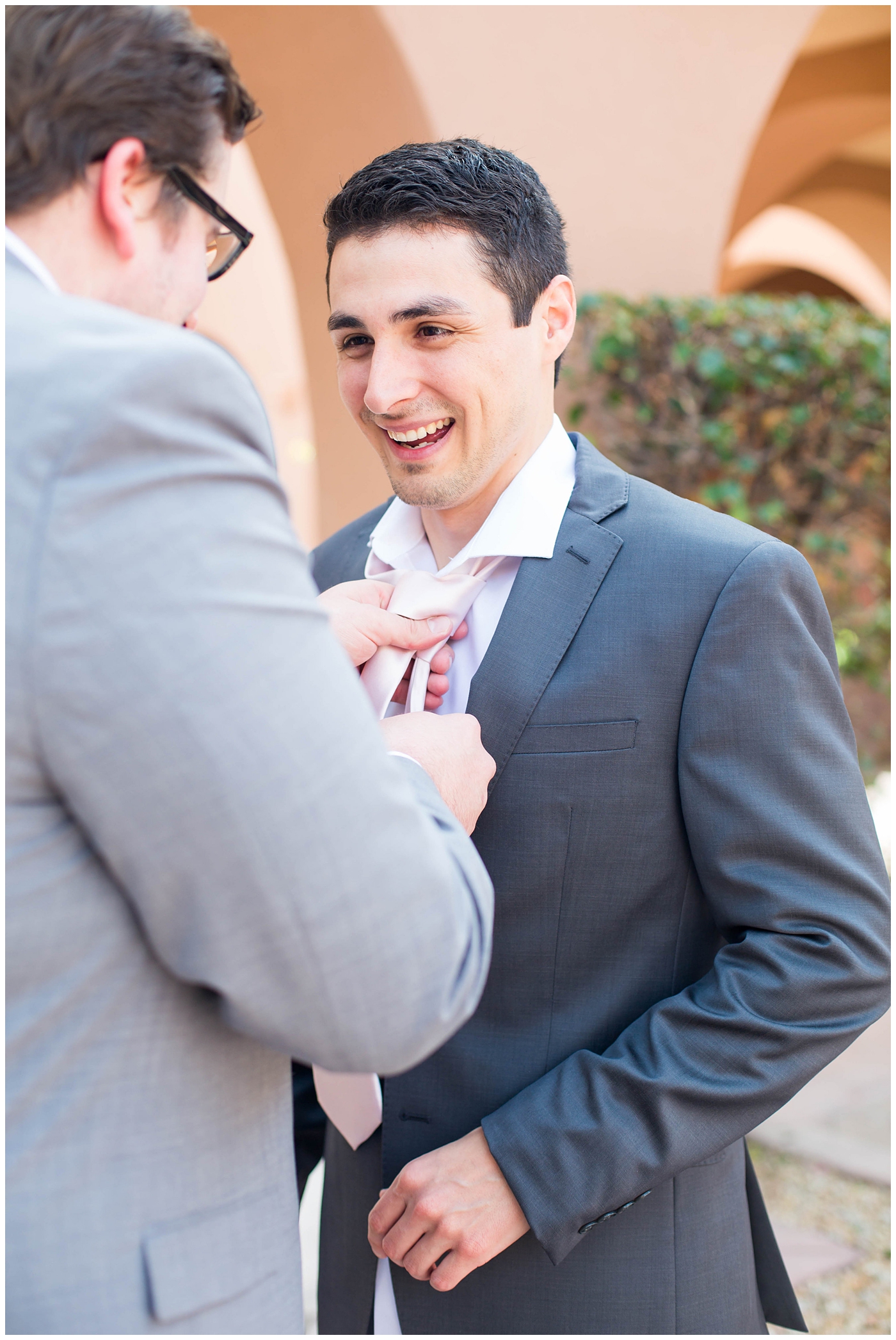 groom in gray suit with pink tie getting ready on wedding day