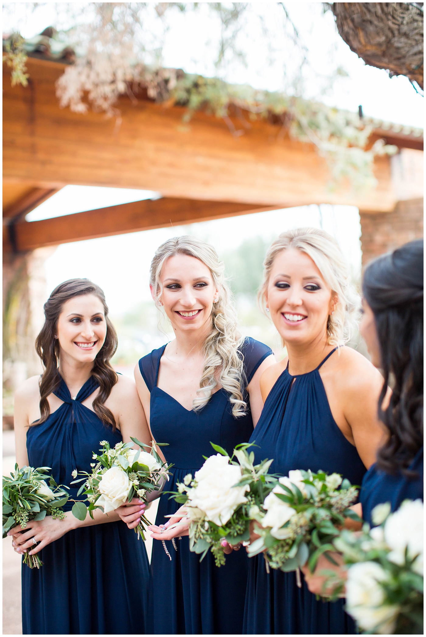 bridesmaids in assorted navy blue dresses with white rose and greenery flower bouquets on wedding day