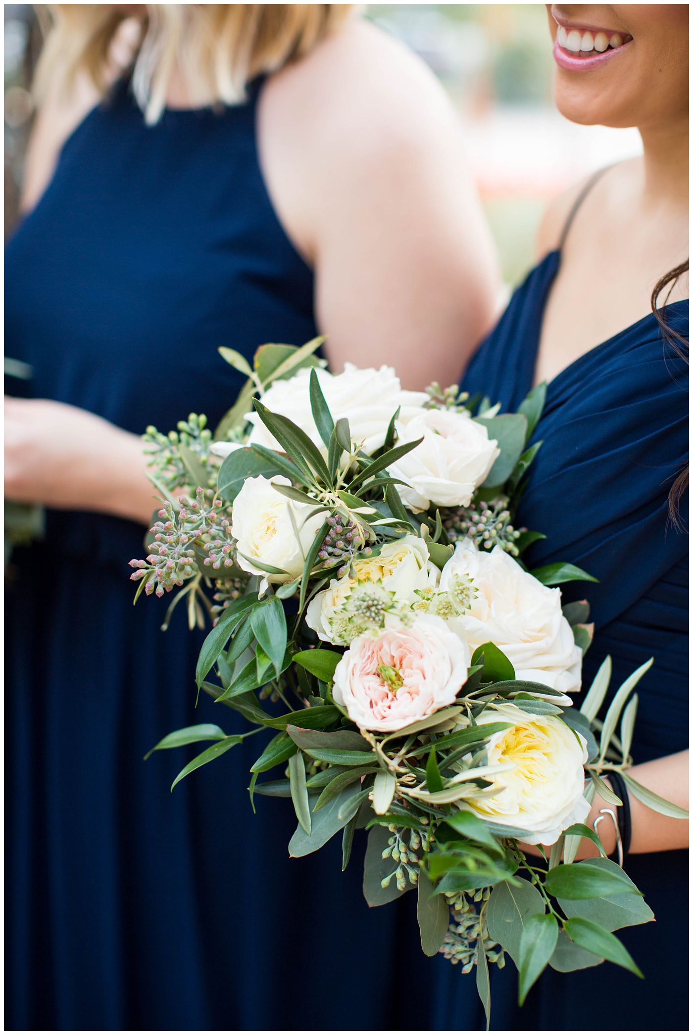 bridesmaids in assorted navy blue dresses with white rose and greenery flower bouquets on wedding day