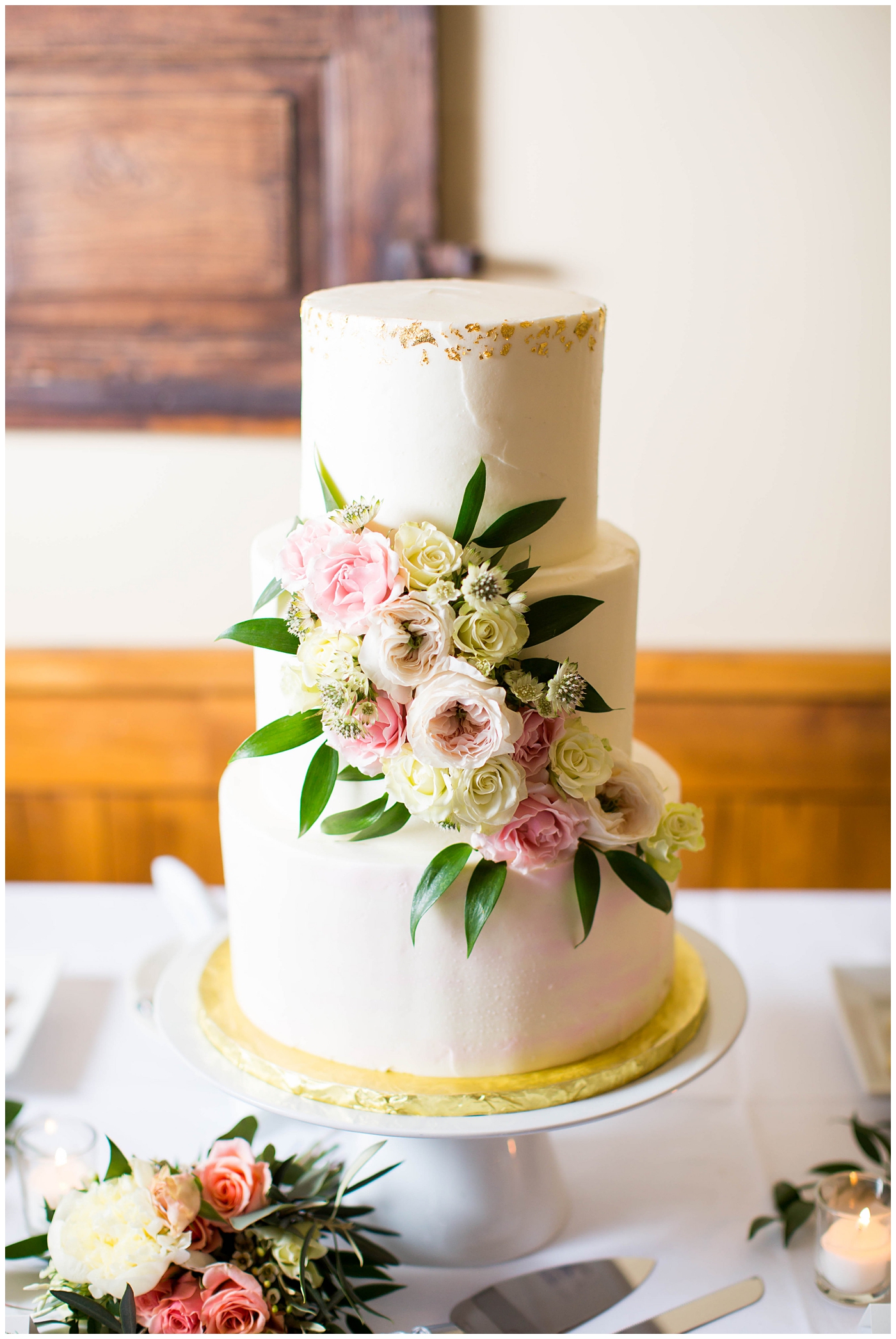 white wedding cake with gold foil and white and pink roses at wedding reception