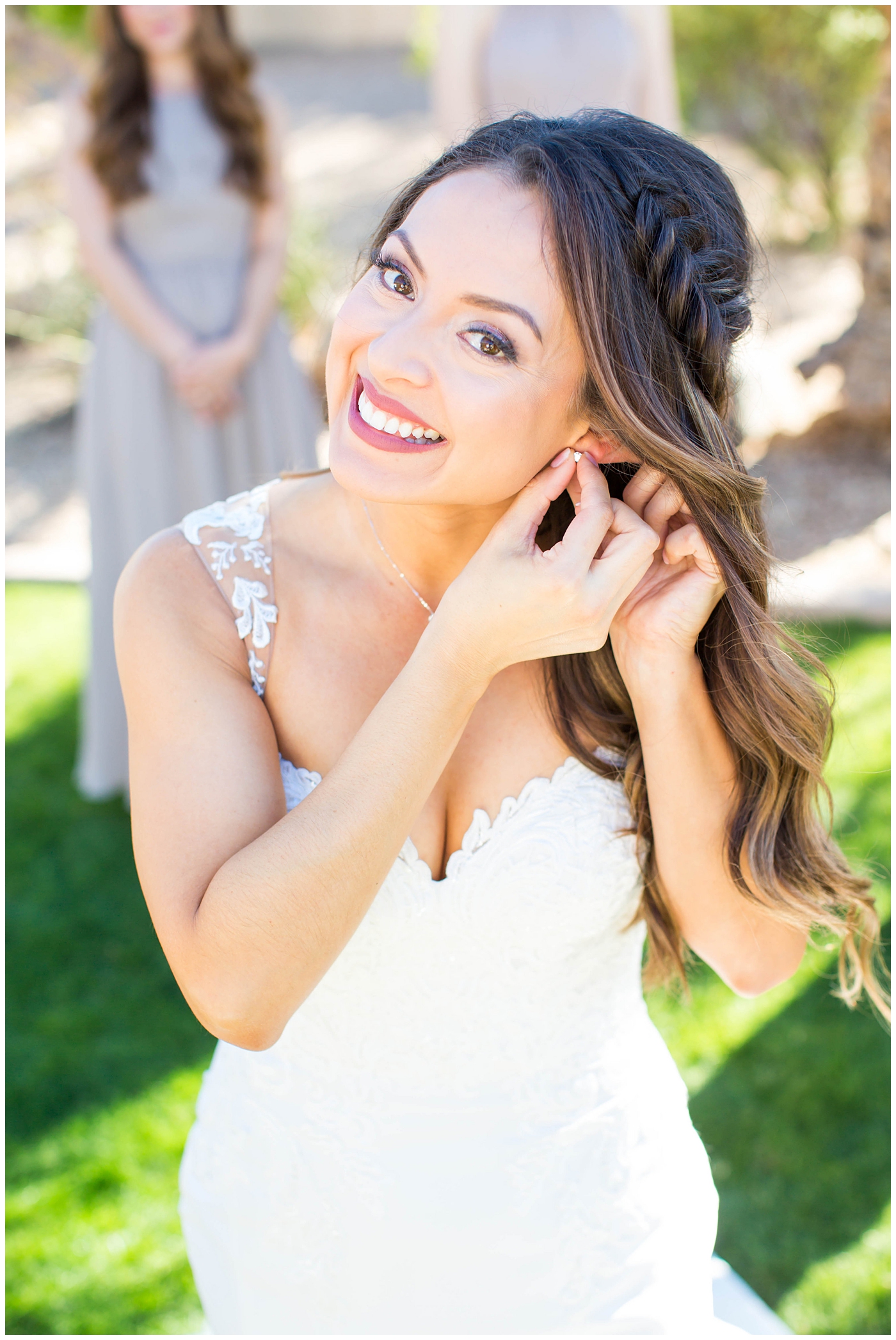 bride in lace cap sleeve wedding dress putting on earrings on wedding day