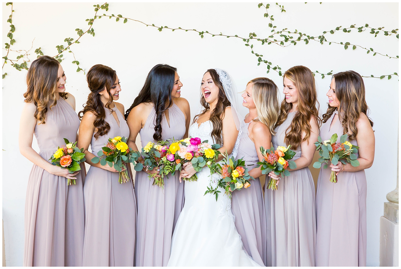 bride in lace cap sleeve wedding dress with bridesmaids in azazie dresses on wedding day with bright pink, yellow and green flower bouquets