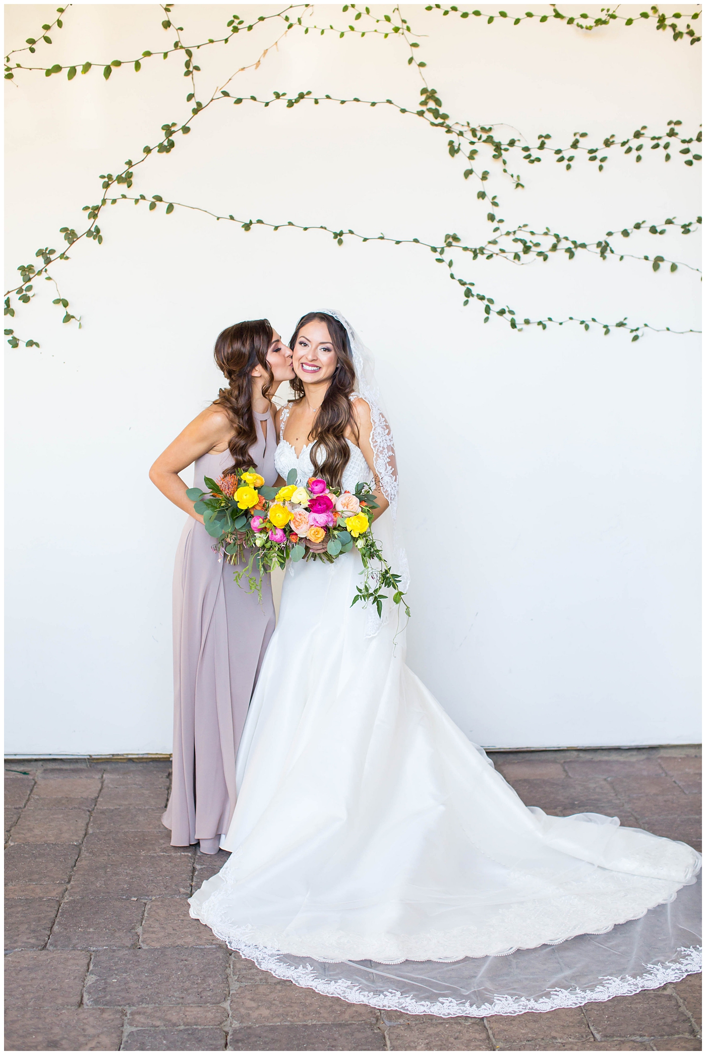 bride in lace cap sleeve wedding dress with bridesmaids in azazie dresses on wedding day with bright pink, yellow and green flower bouquets