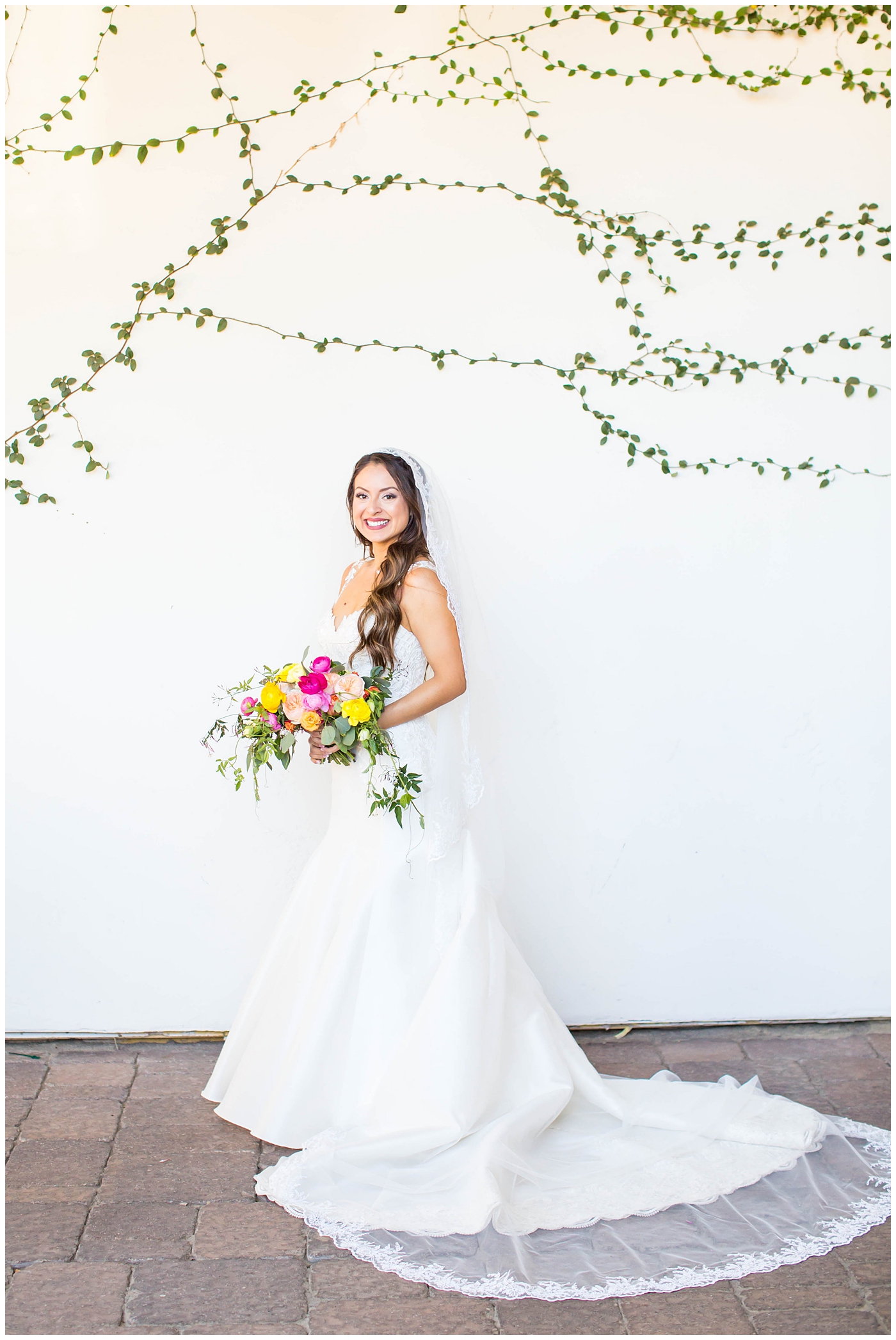 bride in lace cap sleeve wedding dress with bright pink, yellow and green flower bouquets bridal portrait