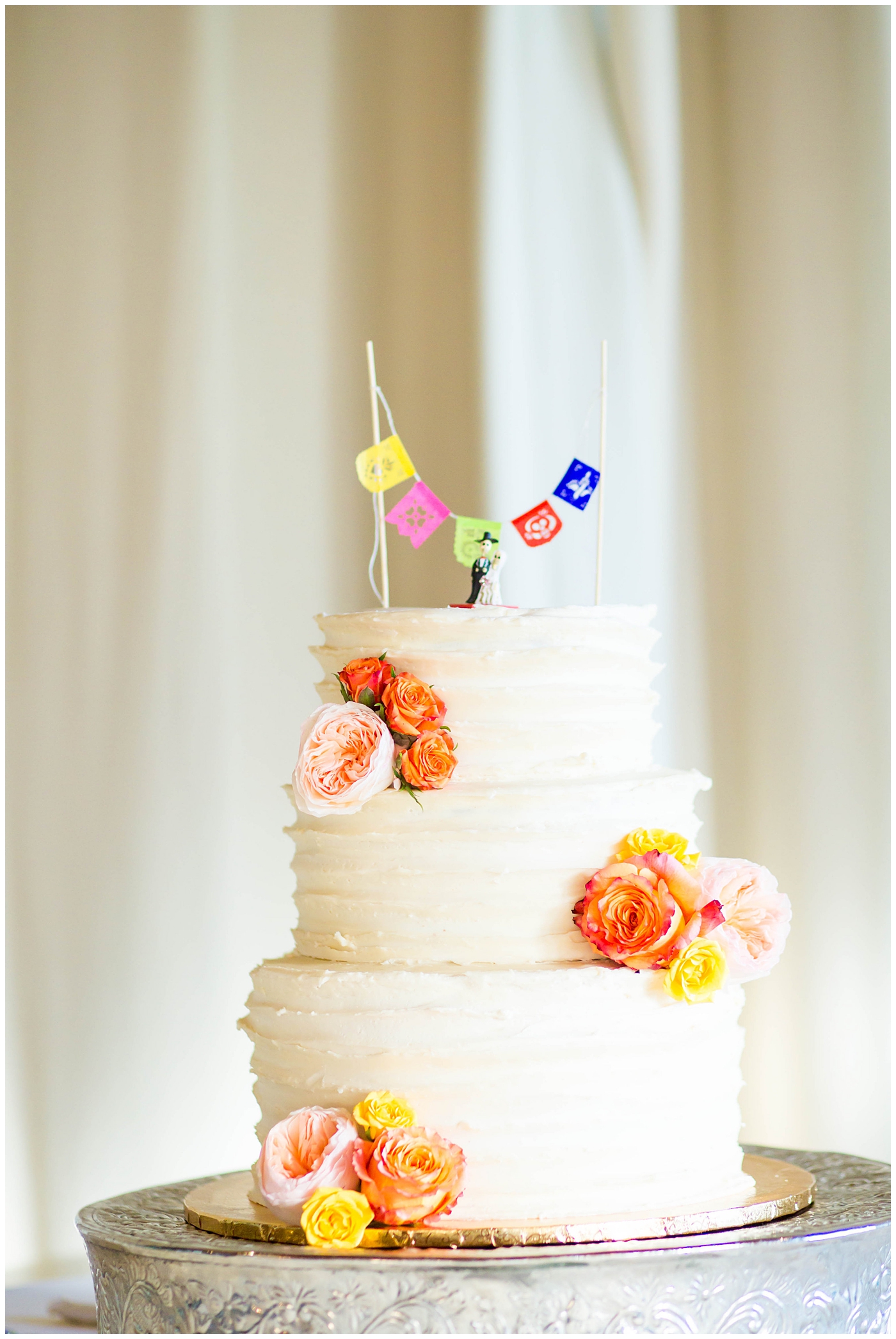 white wedding cake with bright orange flowers and dia de los muertos mr. and mrs. statue cake topper