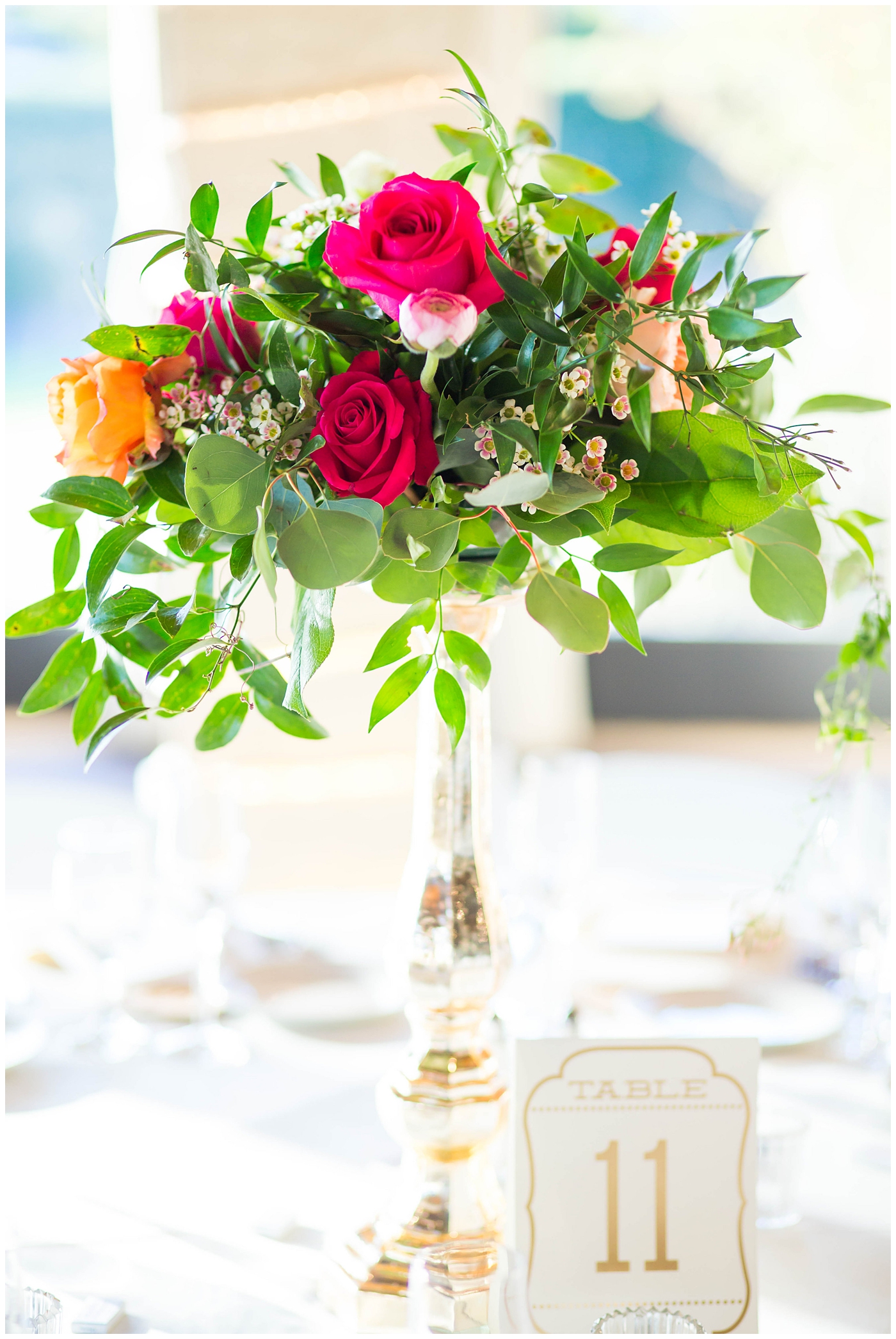 wedding reception details with white tables and chairs with gold stands with white, bright pink, orange, yellow and green flowers
