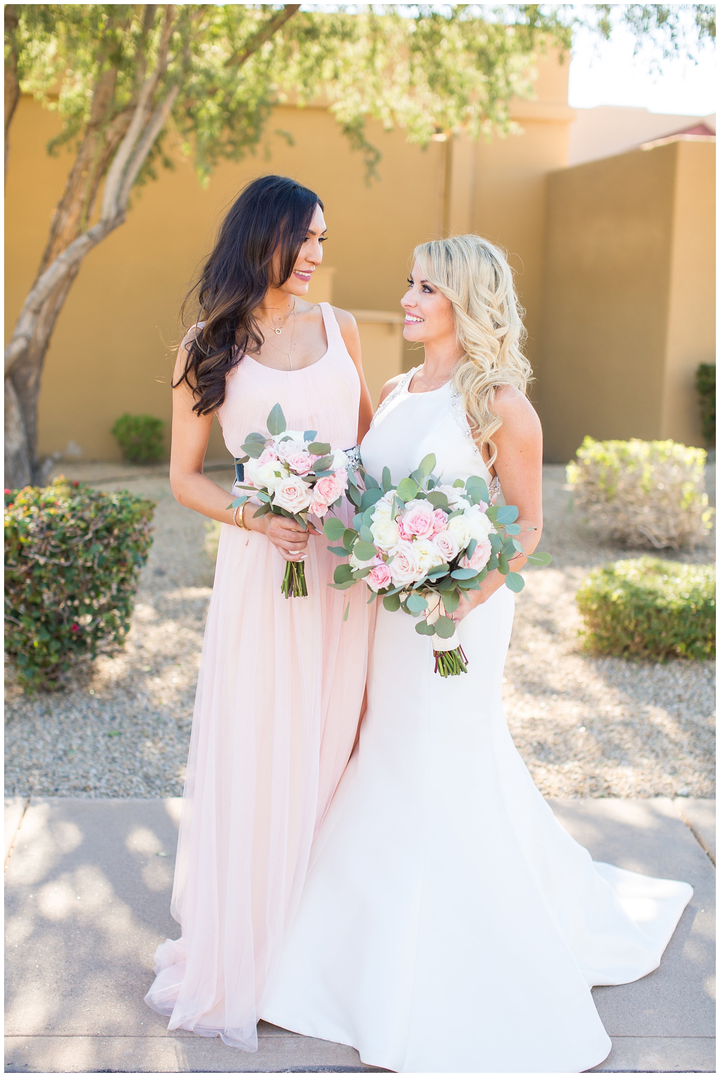 gorgeous bride with side swept hair in racerback pronovias dress and blush pink, white rose and eucalyptus greenery wedding bouquet with bridal party bridesmaids in blush pink dresses on wedding day