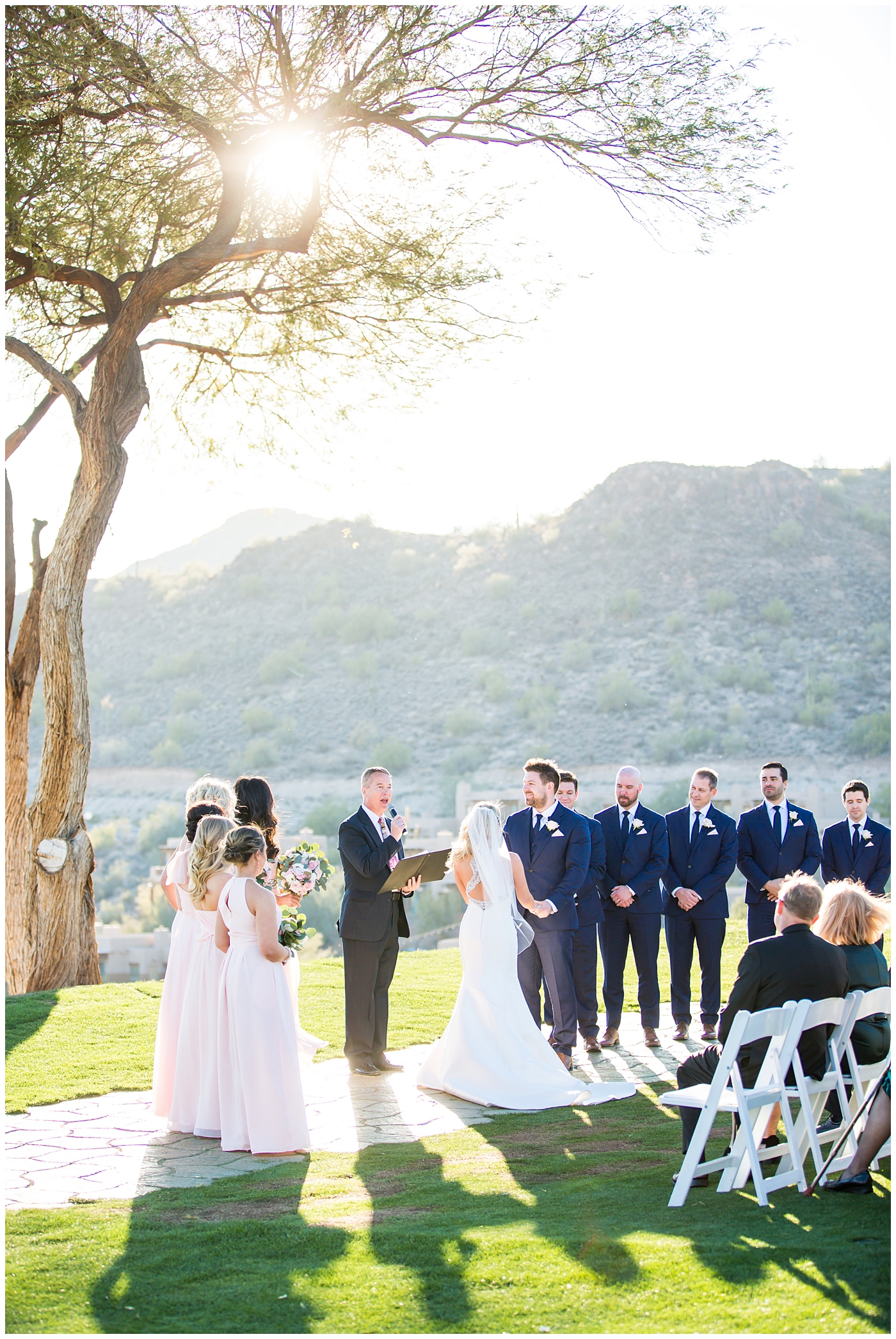 gorgeous bride with side swept hair in racerback pronovias dress and blush pink, white rose and eucalyptus greenery wedding bouquet with groom in navy suit and tie couple portrait at wedding ceremony outside