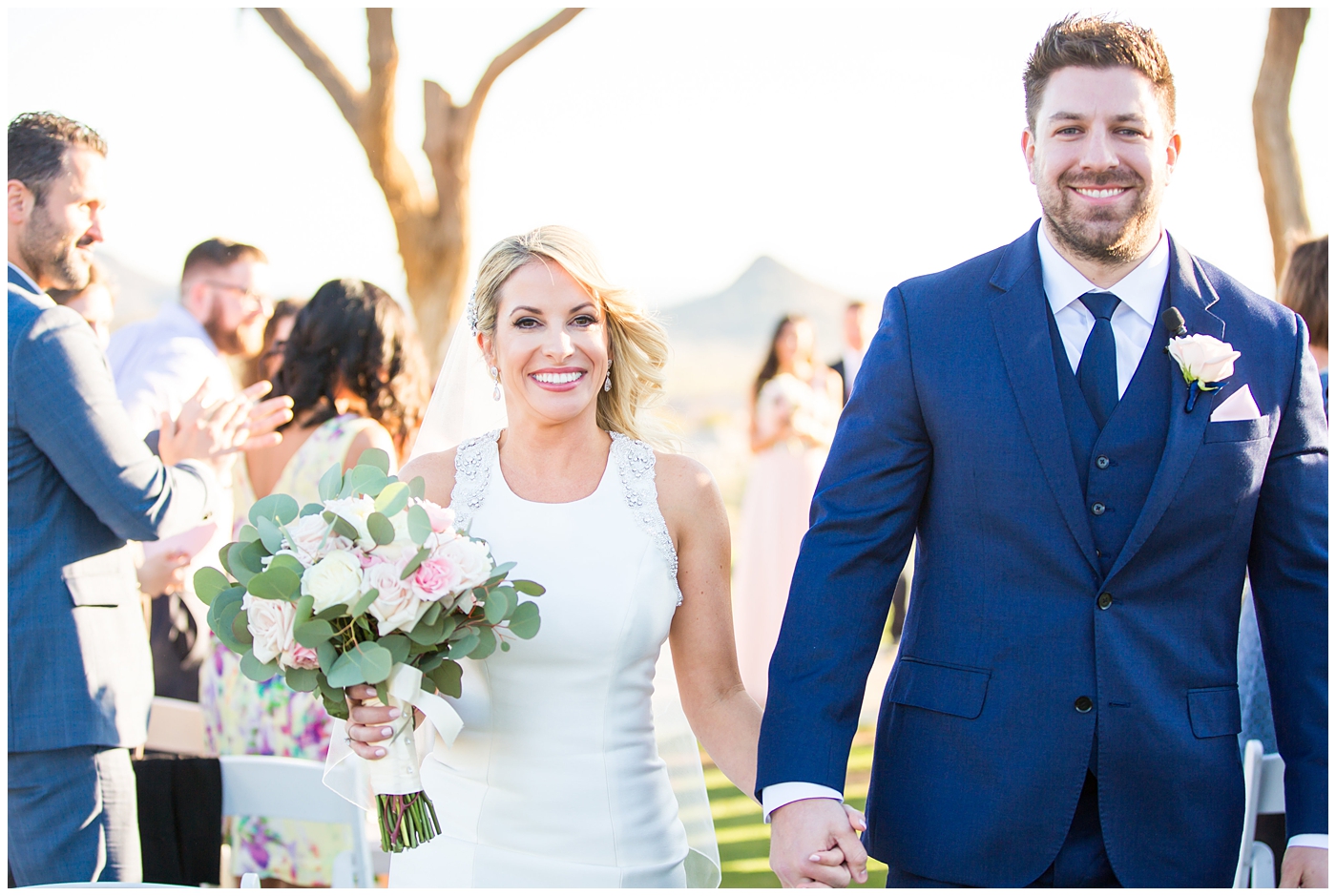 gorgeous bride with side swept hair in racerback pronovias dress and blush pink, white rose and eucalyptus greenery wedding bouquet with groom in navy suit and tie couple portrait at wedding ceremony outside