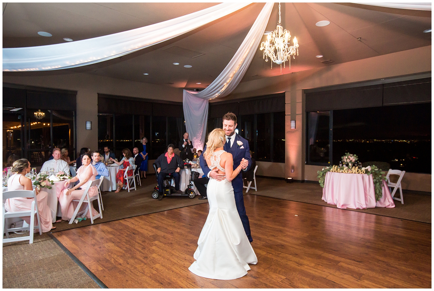 gorgeous bride with side swept hair in racerback pronovias dress and blush pink, white rose and eucalyptus greenery wedding bouquet with groom in navy suit and tie first dance at wedding reception in ballroom