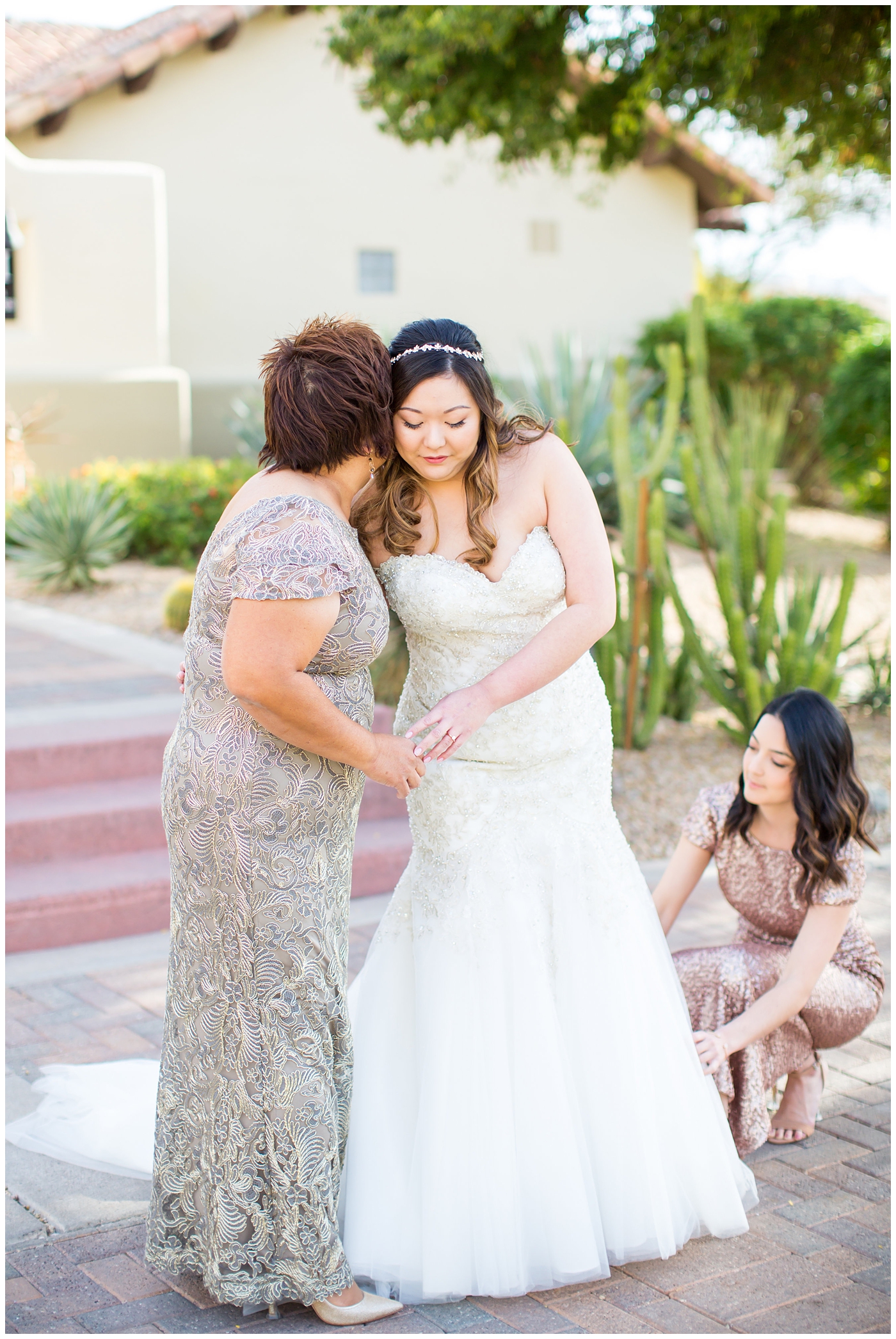 bride getting into strapless wedding dress with beads and shiny sparkle tool with help of mother and bridesmaid in pink sequin dress on wedding day