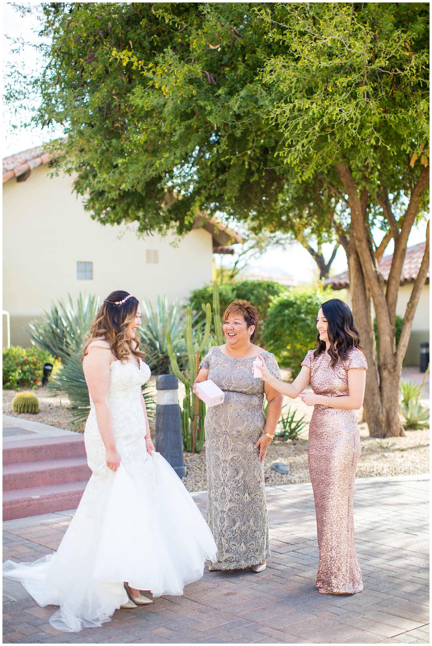 bride in strapless wedding dress with beads and shiny sparkle tool getting ready with help of mother and bridesmaid in pink sequin dress on wedding day