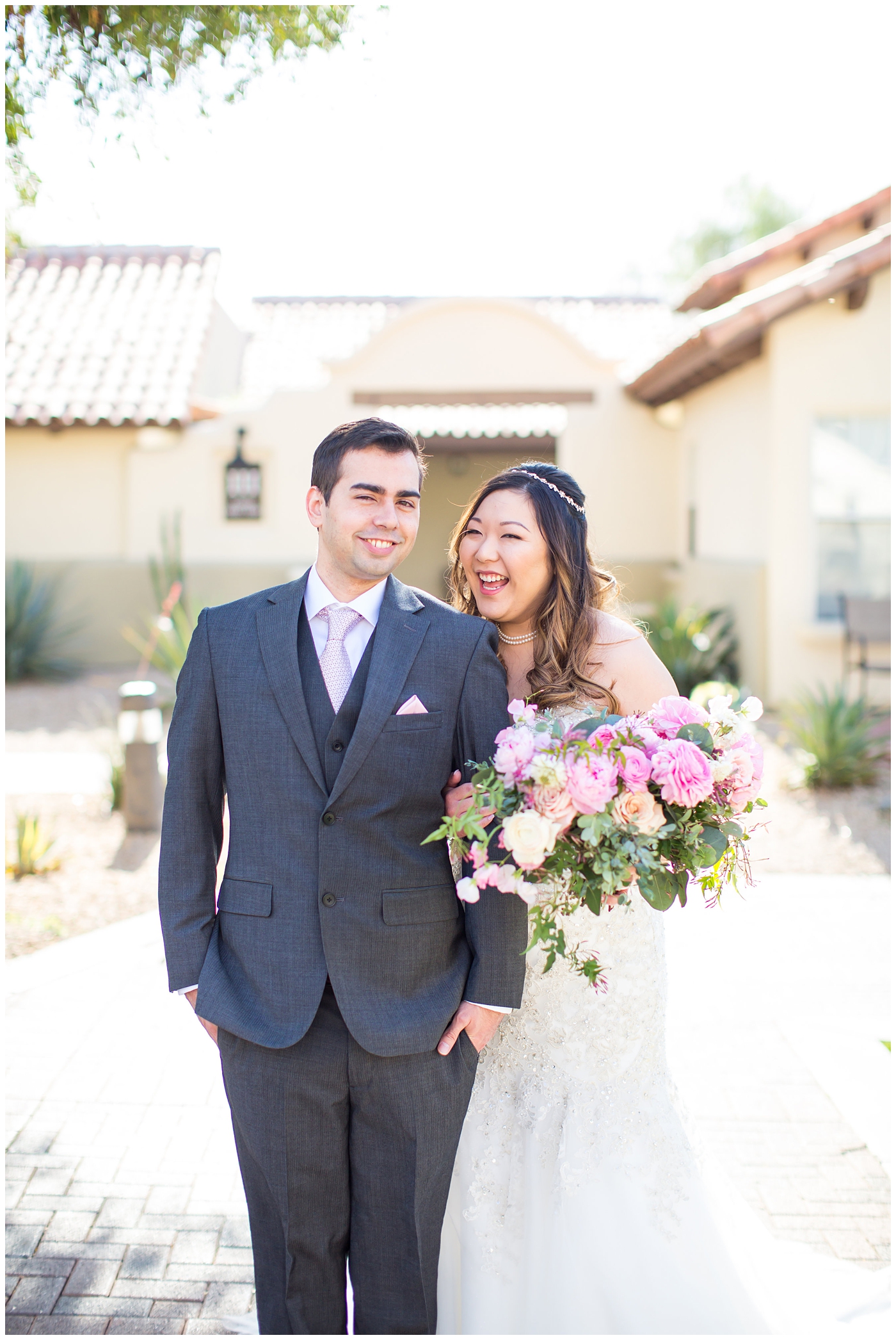 bride in strapless wedding dress with beads and shiny sparkle tool holding pink peony, roses, light coral rose and loose greenery bridal bouquet with groom in gray suit with silver tie on wedding day portrait