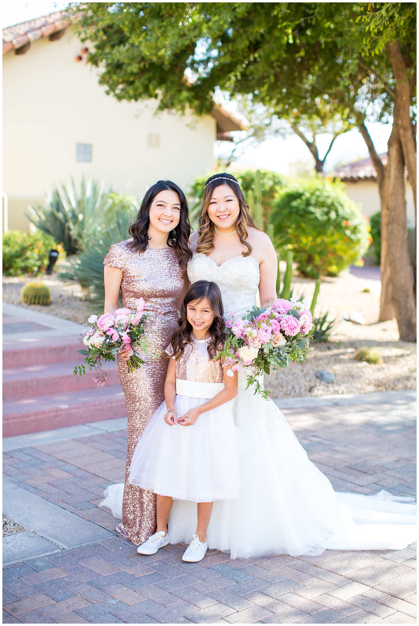 bride in strapless wedding dress with beads and shiny sparkle tool holding pink peony, roses, light coral rose and loose greenery bridal bouquet with bridesmaid in pink sequin dress and flower girl in sneakers on wedding day portrait