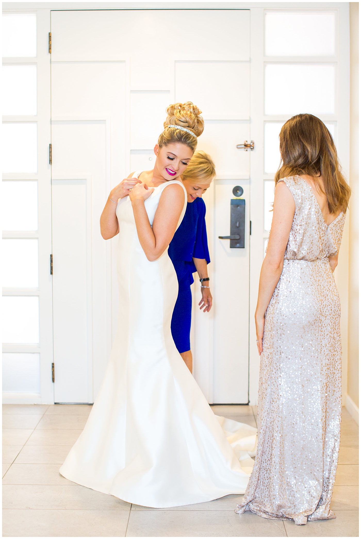 Bride in sareh nouri wedding dress with bow on the back and pink lip stick with all white flower bouquet with bridesmaid in sequin gold dress getting ready