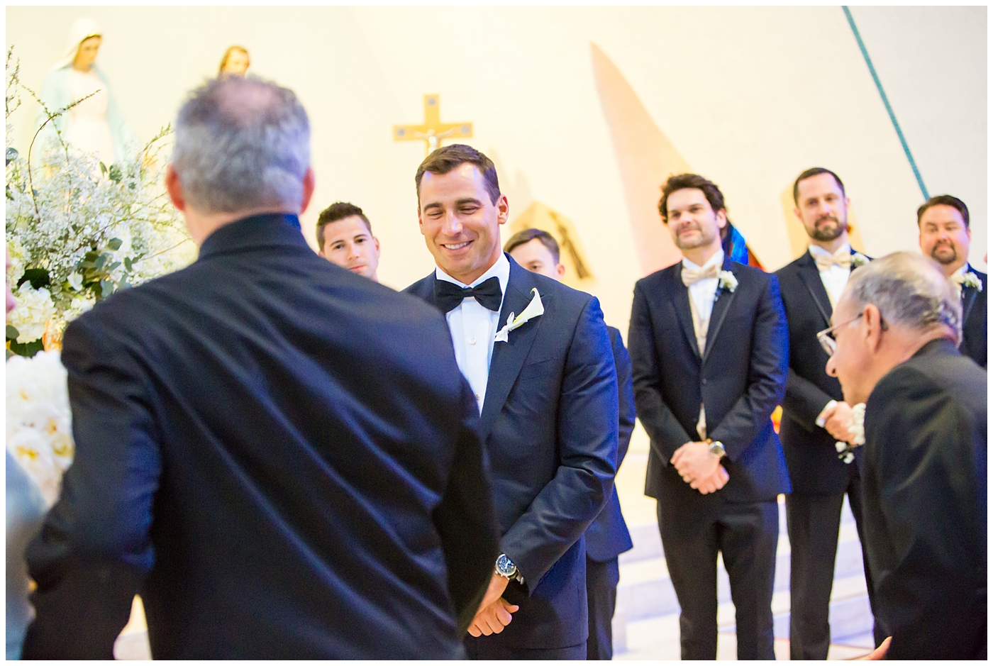 groom in navy neiman marcus and canali suit with blue bowtie with calla lilly boutonniere seeing bride walk down aisle at church wedding ceremony