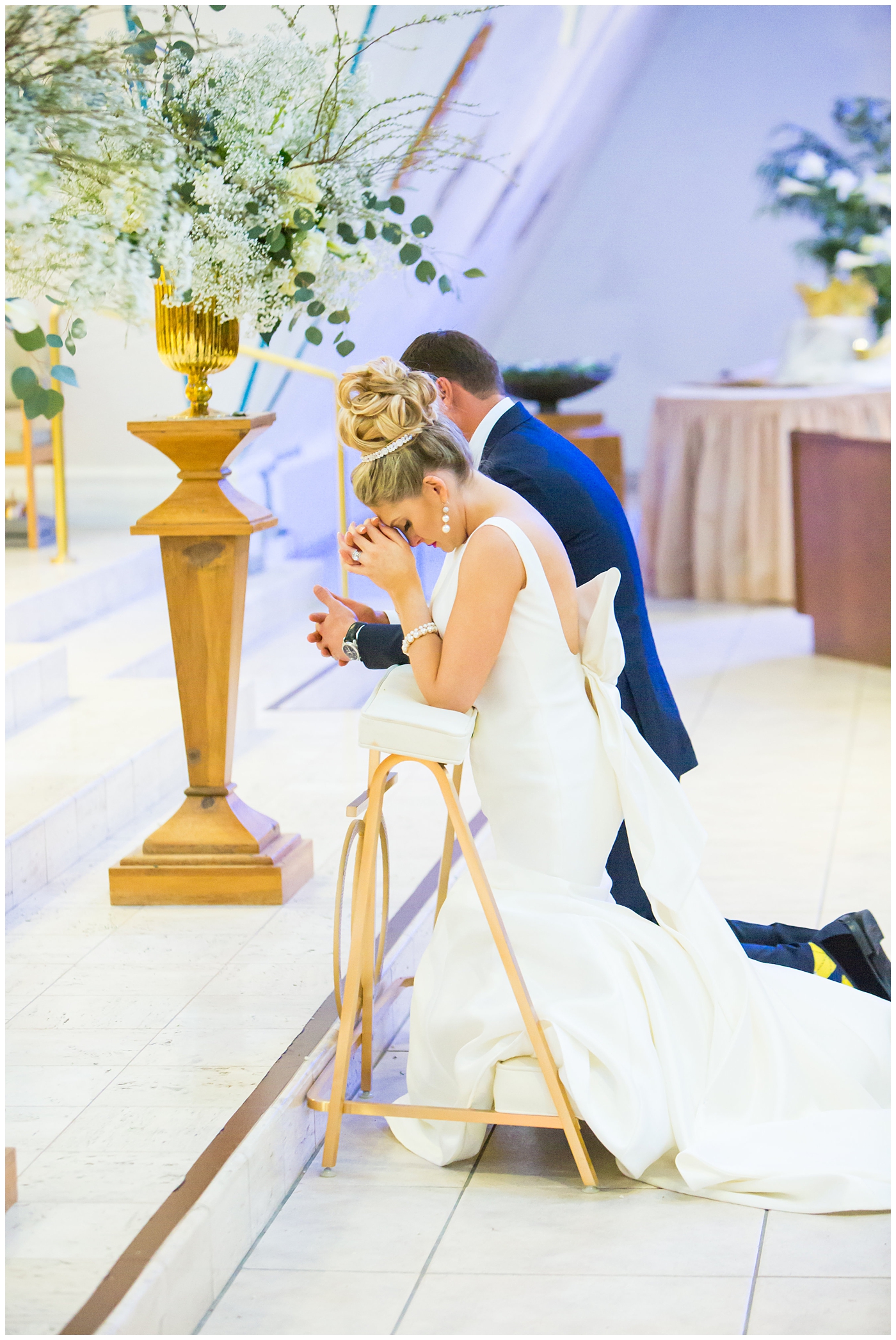 Bride in sareh nouri wedding dress with bow on the back and pink lip stick with all white flower bouquet with groom in navy neiman marcus and canali suit with bowtie with calla lilly boutonniere at church wedding ceremony