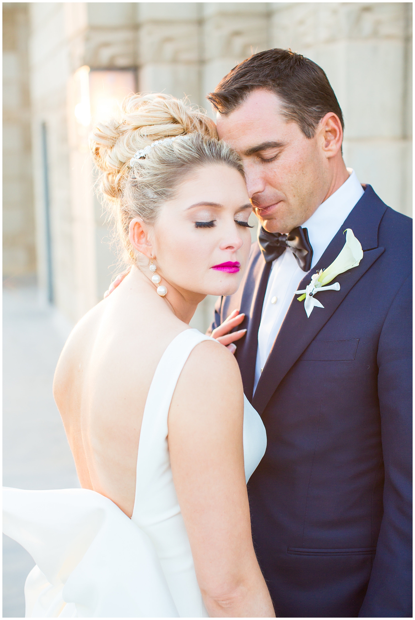 Bride in sareh nouri wedding dress with bow on the back and pink lip stick with all white flower bouquet with groom in navy neiman marcus and canali suit with bowtie with calla lilly boutonniere wedding day portrait