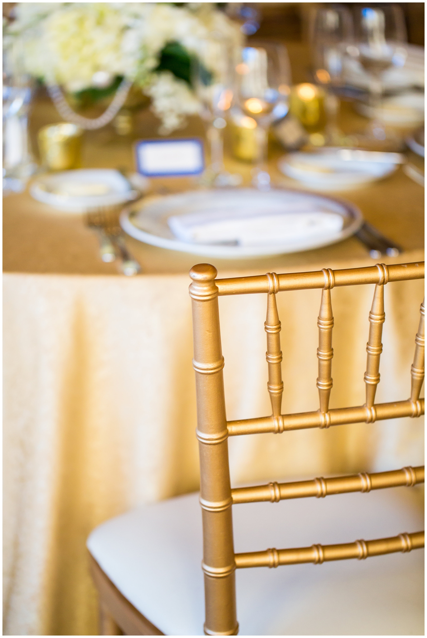Arizona Biltmore gold ballroom wedding reception details with gold chairs and tablecloths with white roses and greenery centerpieces in gold vases with glitter royal blue placecards