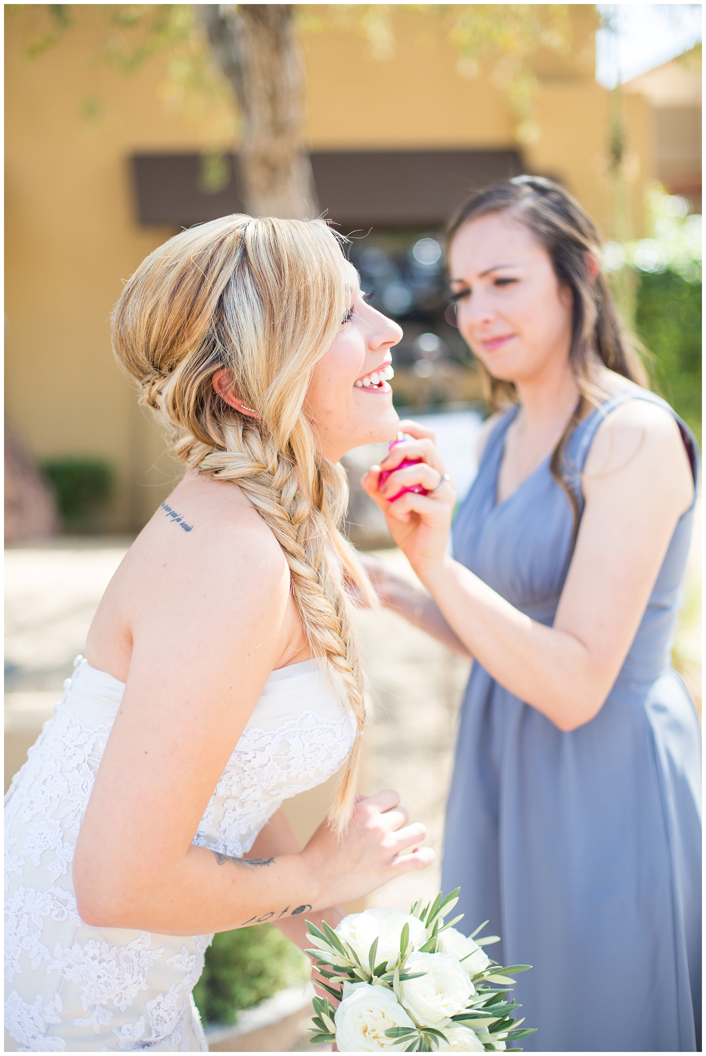 bride with fishtail braid and strapless dress with white rose and greenery bouquet with bridesmaids in slate gray long dresses getting ready on wedding day