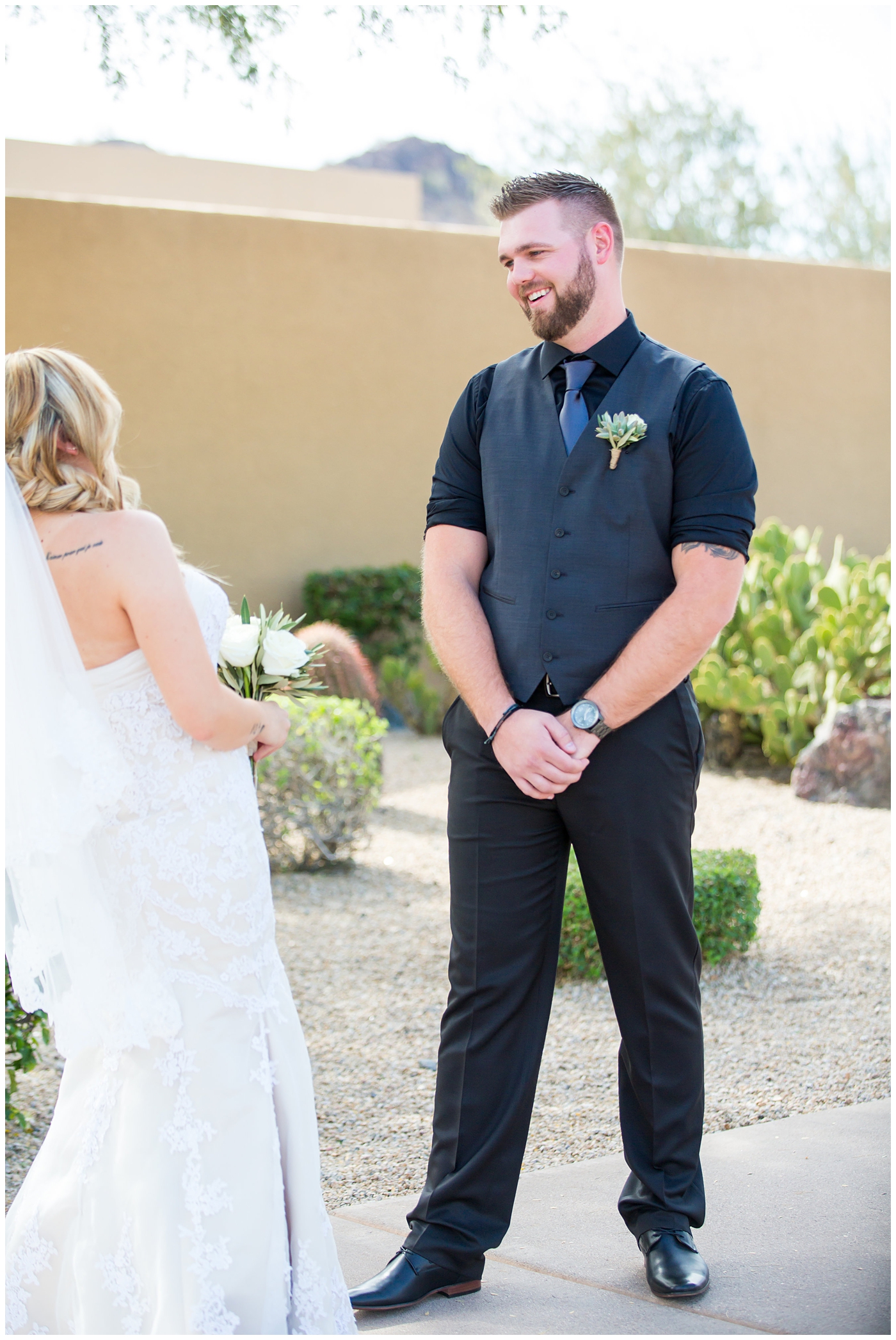 bride with fishtail braid and strapless dress with white rose and greenery bouquet with groom in black pants and vest and tie with rolled up shirt sleeves with succulent boutonniere wedding day first look portrait