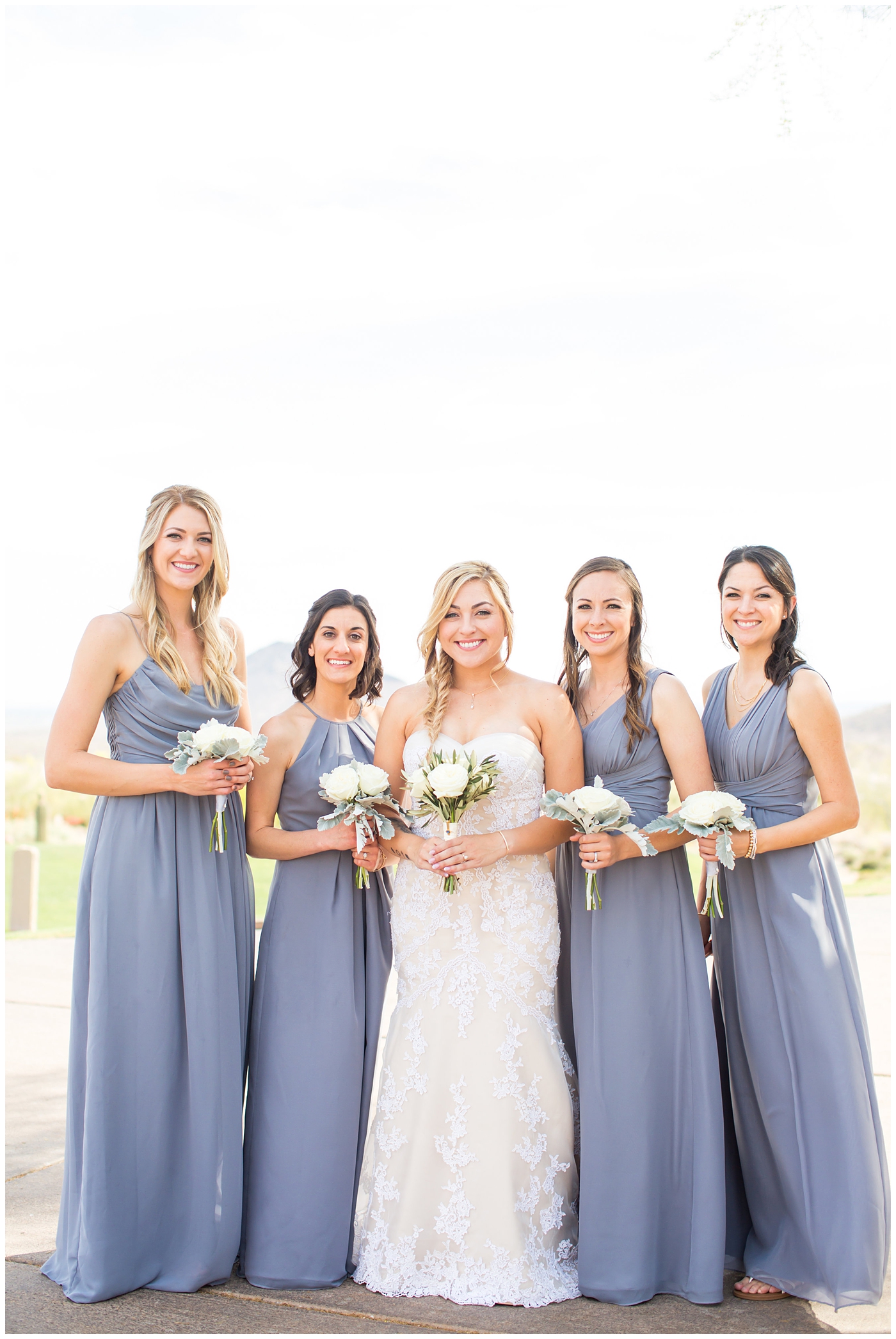 bride with fishtail braid and strapless dress with white rose and greenery bouquet with bridesmaids in slate gray long dresses on wedding day bridal party portrait