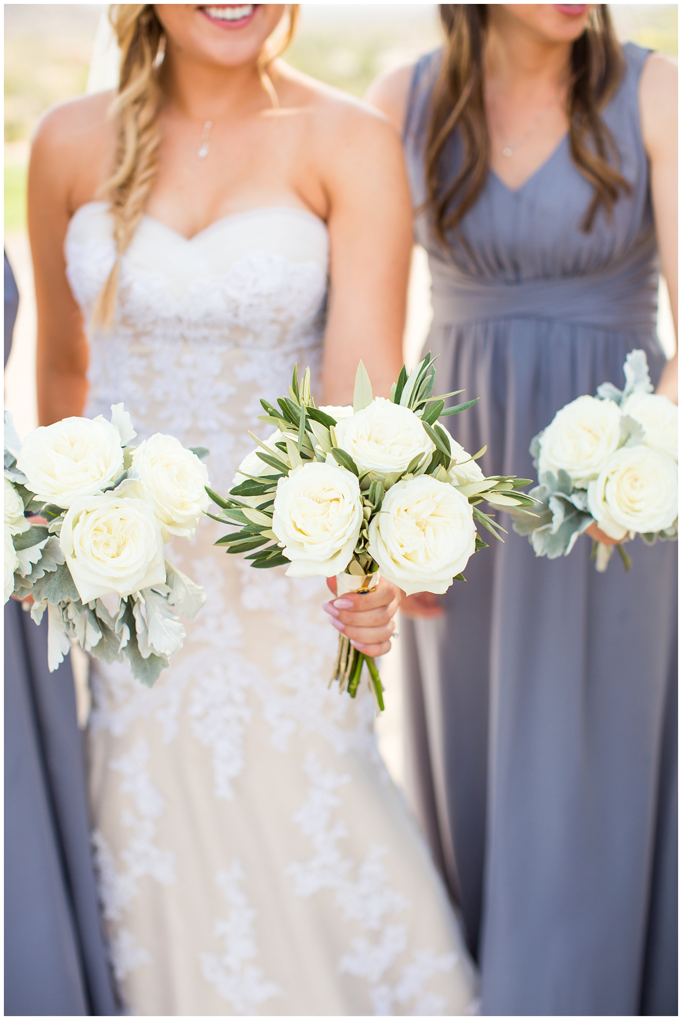 bride with fishtail braid and strapless dress with white rose and greenery bouquet with bridesmaids in slate gray long dresses on wedding day bridal party portrait