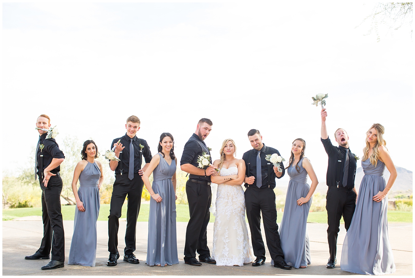 bride with fishtail braid and strapless dress with white rose and greenery bouquet with bridesmaids in slate gray long dresses with groom in black pants and vest and tie with rolled up shirt sleeves with succulent boutonniere with groomsmen in black pants with suspenders and tie wedding day bridal party portrait